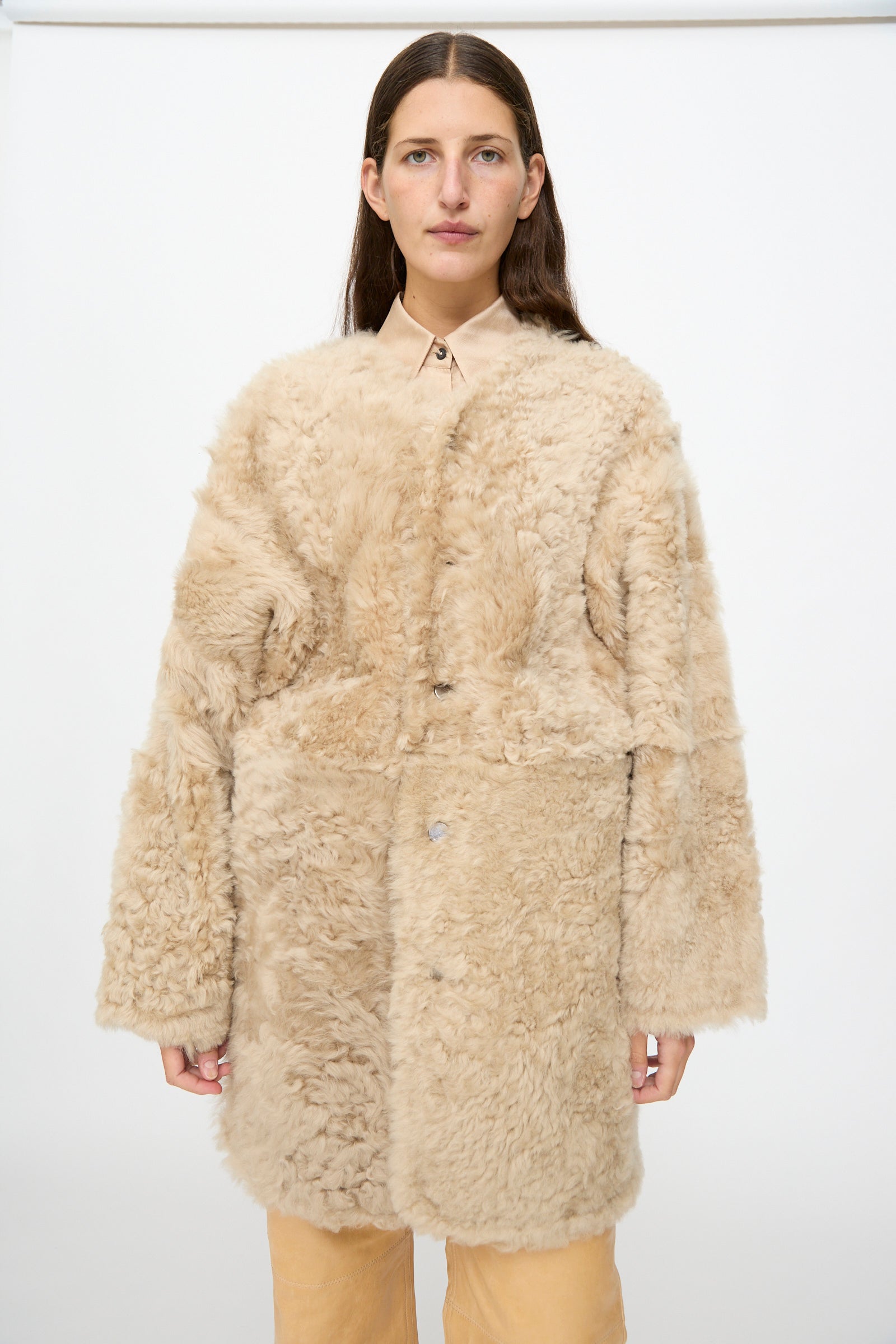 A woman wearing the Milena Silvano Sheepskin Reversible Liner in Oat over a collared shirt and tan pants stands against a plain white background.