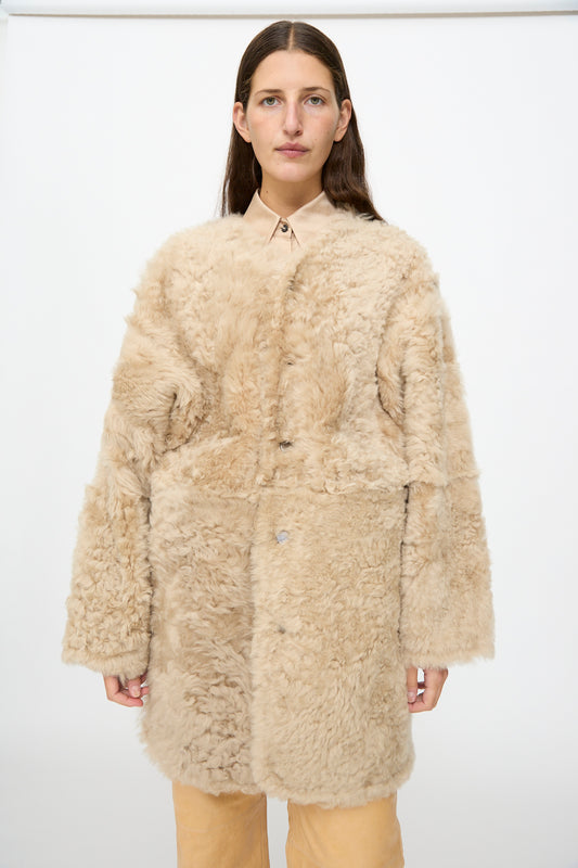A woman wearing the Milena Silvano Sheepskin Reversible Liner in Oat over a collared shirt and tan pants stands against a plain white background.