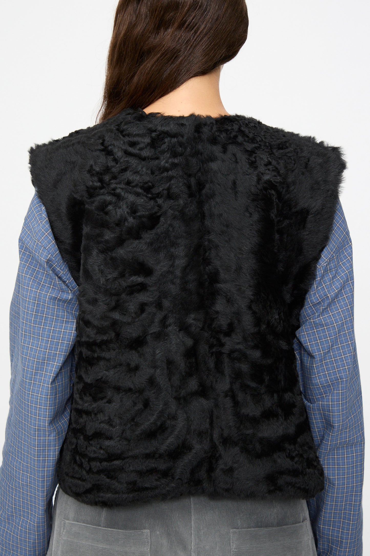 A person seen from behind wearing the Milena Silvano Sheepskin Transition Vest in Black over a blue plaid shirt and gray pants.