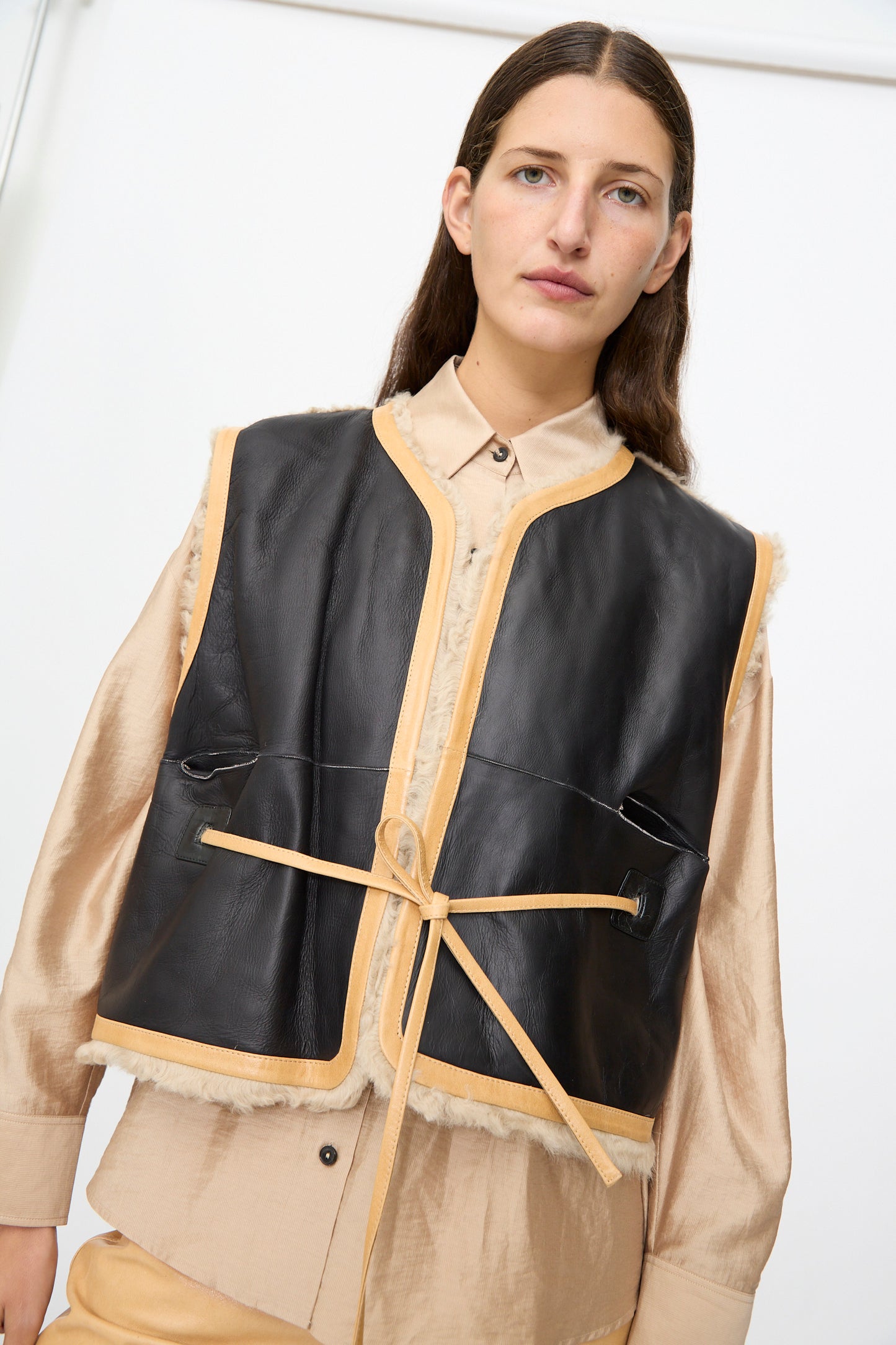 A person wearing the Milena Silvano Sheepskin Transition Vest in Oat layered over a beige button-up shirt, looking at the camera against a plain white background.