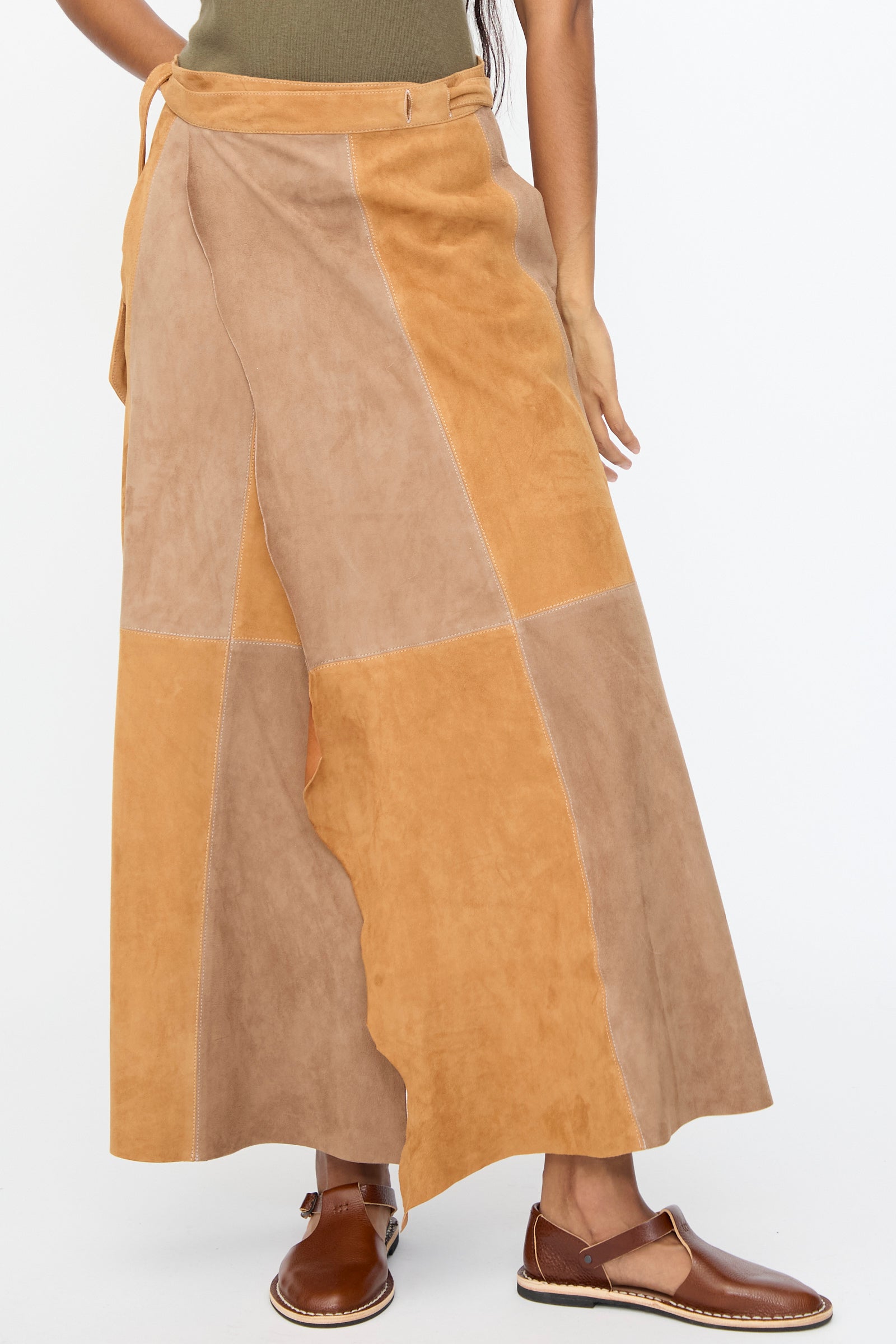 A person wearing the Milena Silvano Suede Persephone Skirt in Cinnamon, paired with an olive top and brown flats, is shown from mid-torso to feet against a plain background.