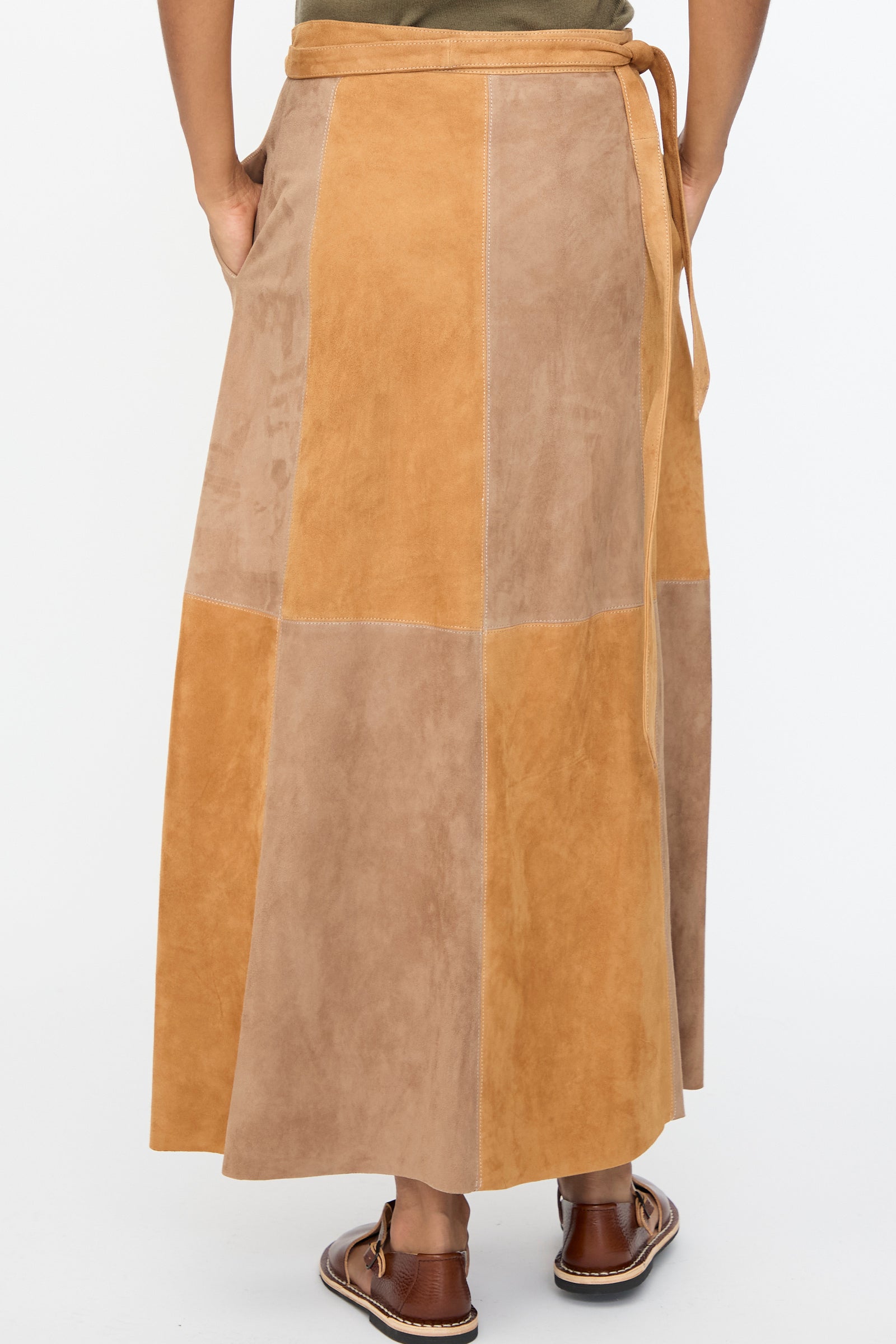 Person shown from the back wearing Milena Silvano’s Suede Persephone Skirt in Cinnamon, a long color-blocked goatskin suede piece in tan and light brown with side pockets, paired with brown sandals.