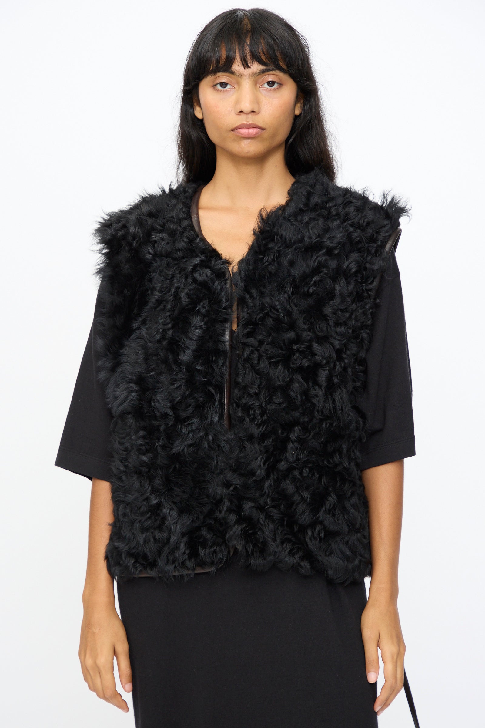 A person stands against a plain background wearing the Milena Silvano Transition Vest in Chaga—a black, textured relaxed-fit vest over a black outfit—looking directly at the camera. 