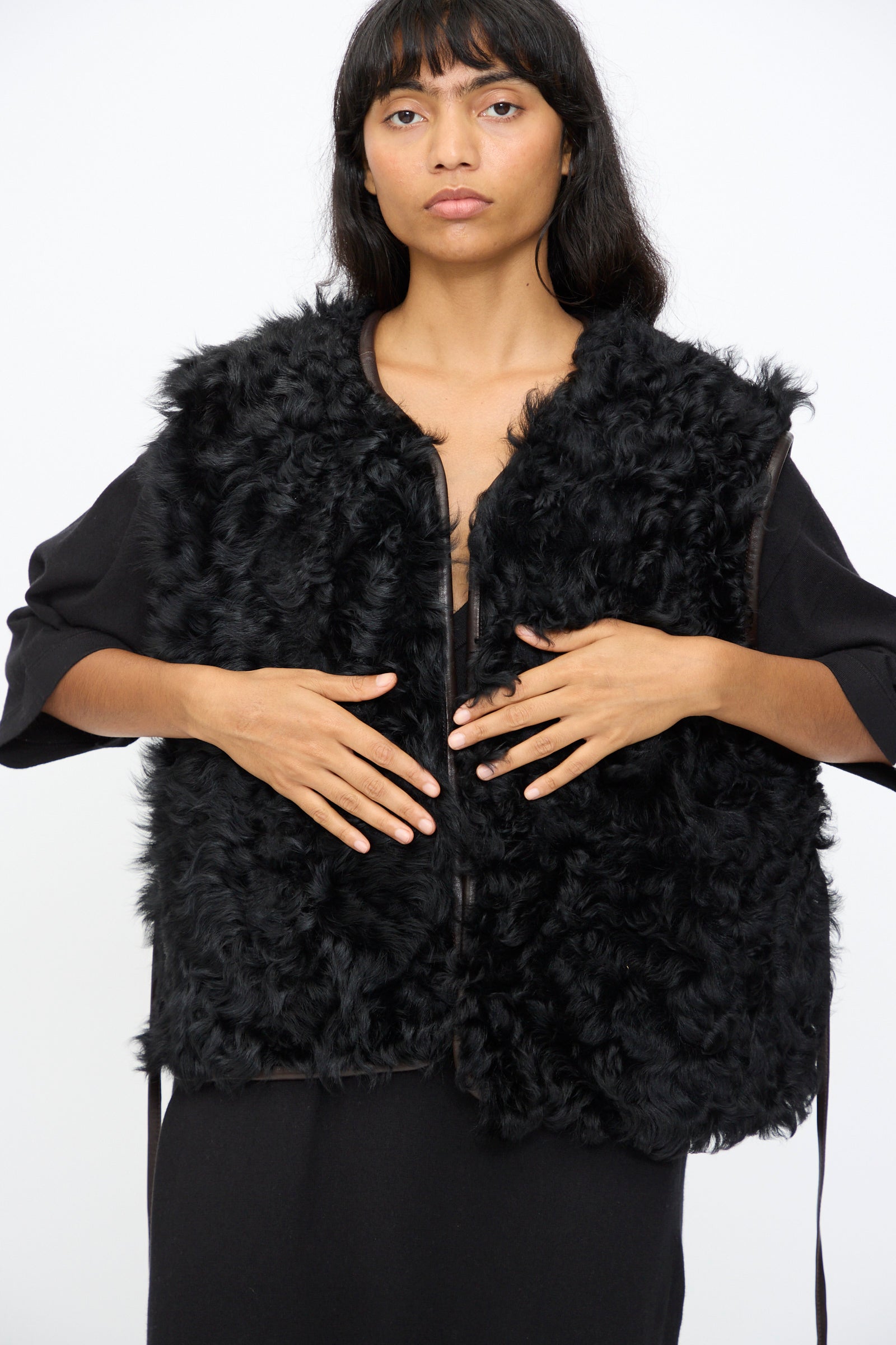 A woman with long dark hair wears the Milena Silvano Transition Vest in Chaga over a black outfit, standing against a plain white background.