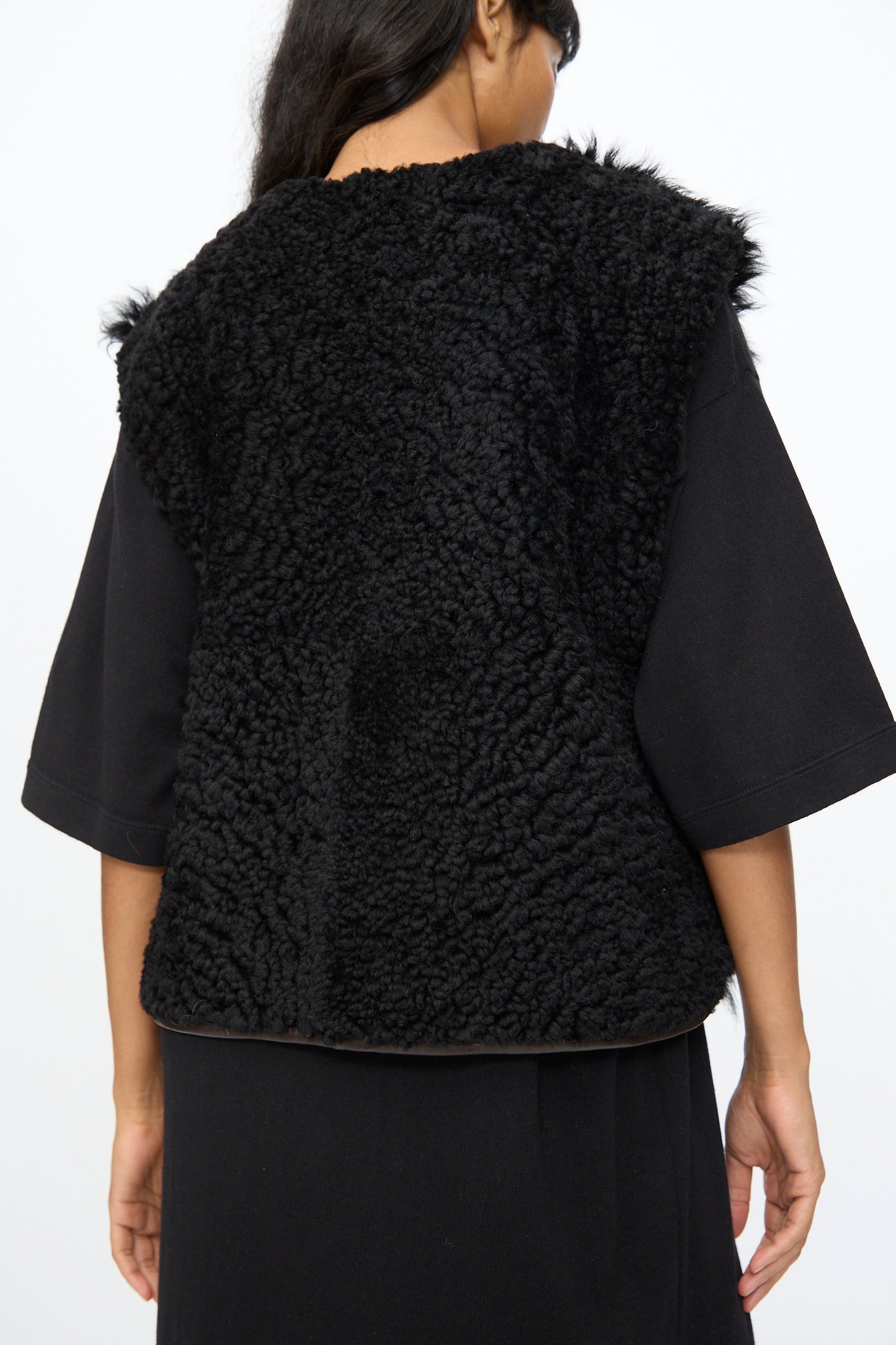 A person shown from the back wears the Milena Silvano Transition Vest in Chaga, layered over a black shirt.