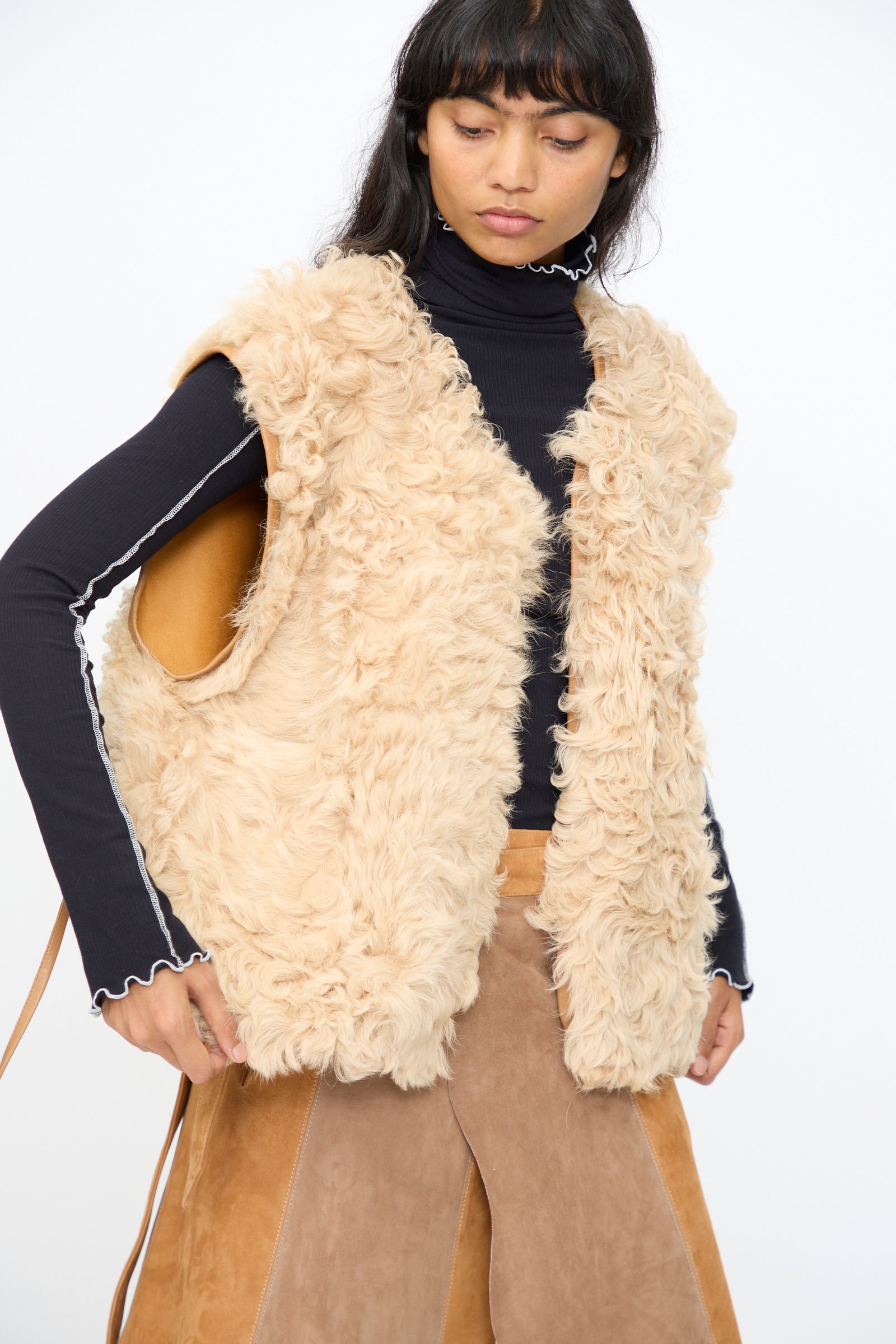 A person wears the Milena Silvano Transition Vest in Oat over a black long-sleeve top and light brown pants, standing against a plain white background.
