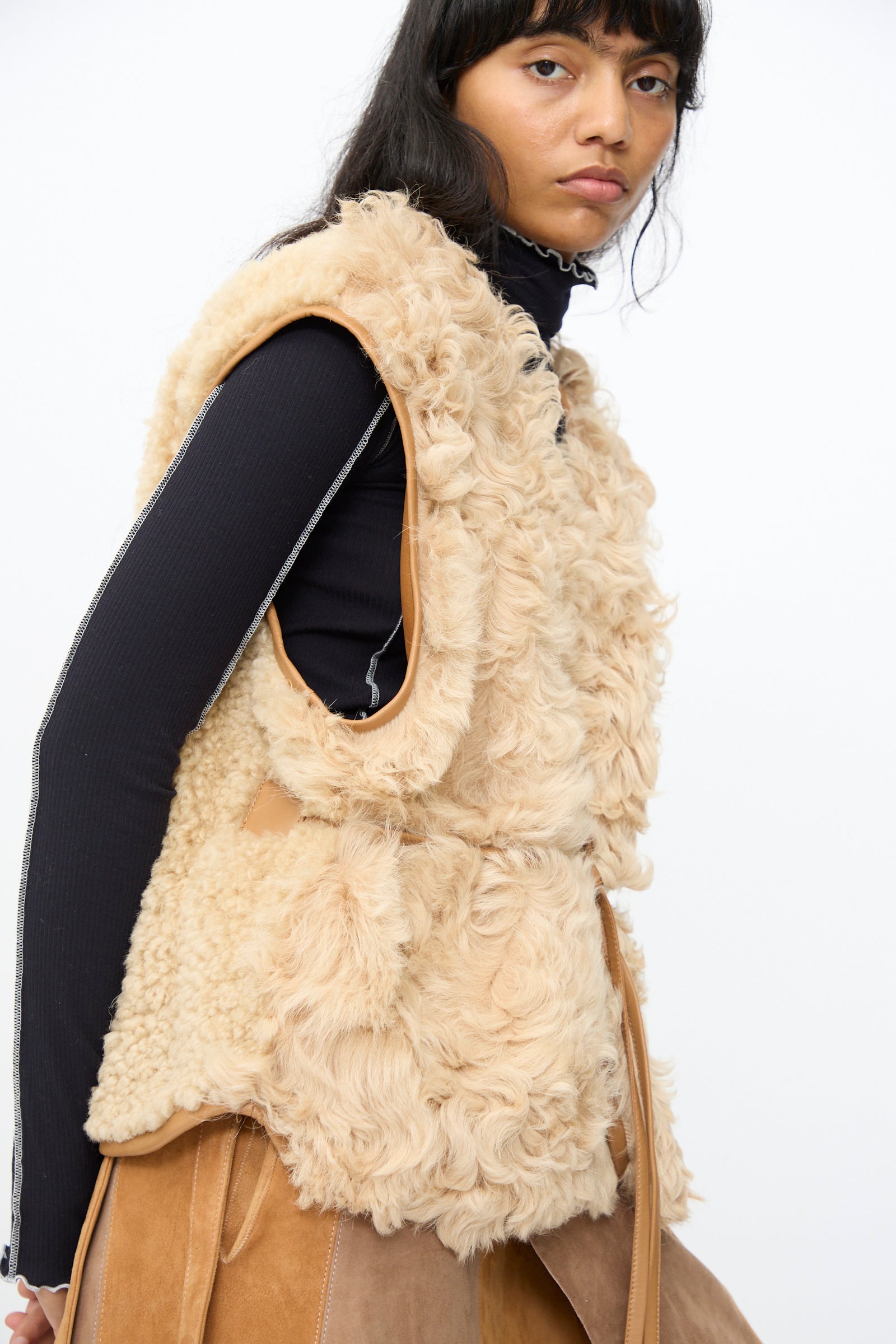 Model wears the Milena Silvano Transition Vest in Oat over a black long-sleeve top, looking at the camera with a neutral expression against a plain background.