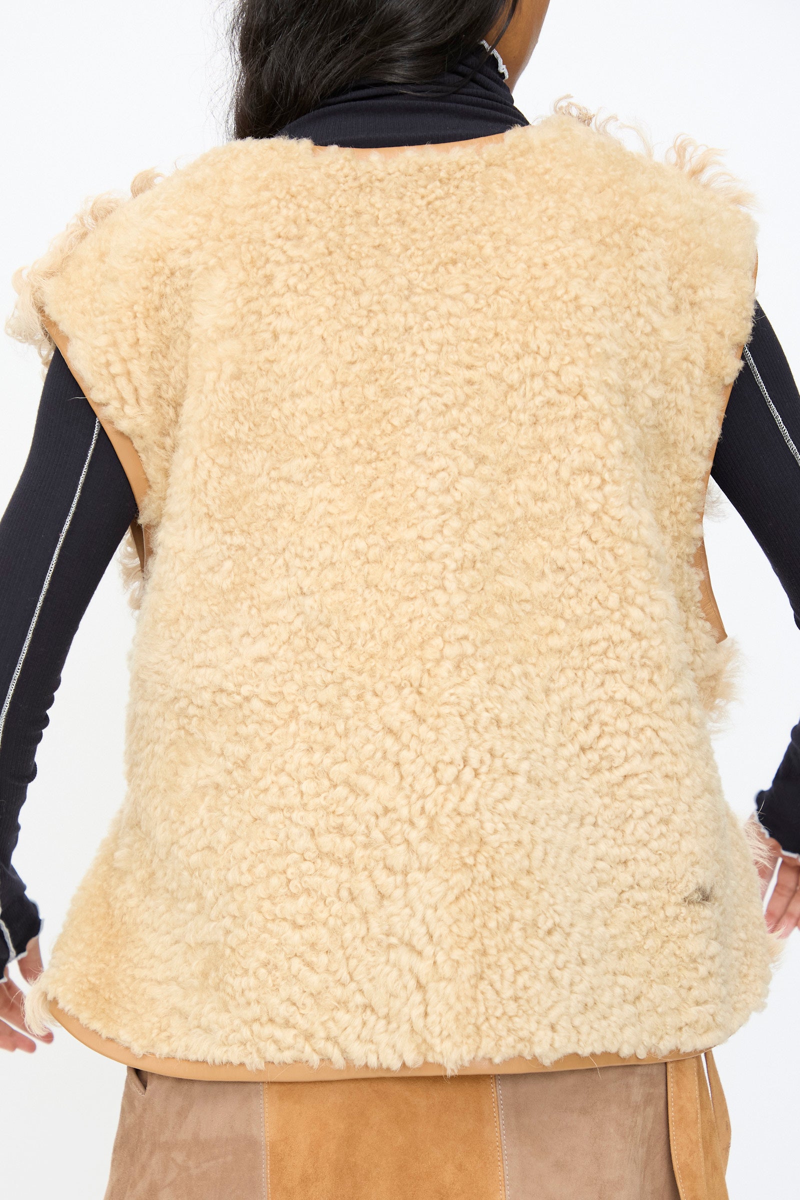 A person shown from the back wears the Milena Silvano Transition Vest in Oat, a beige sleeveless relaxed fit style, layered over a black long-sleeve top.