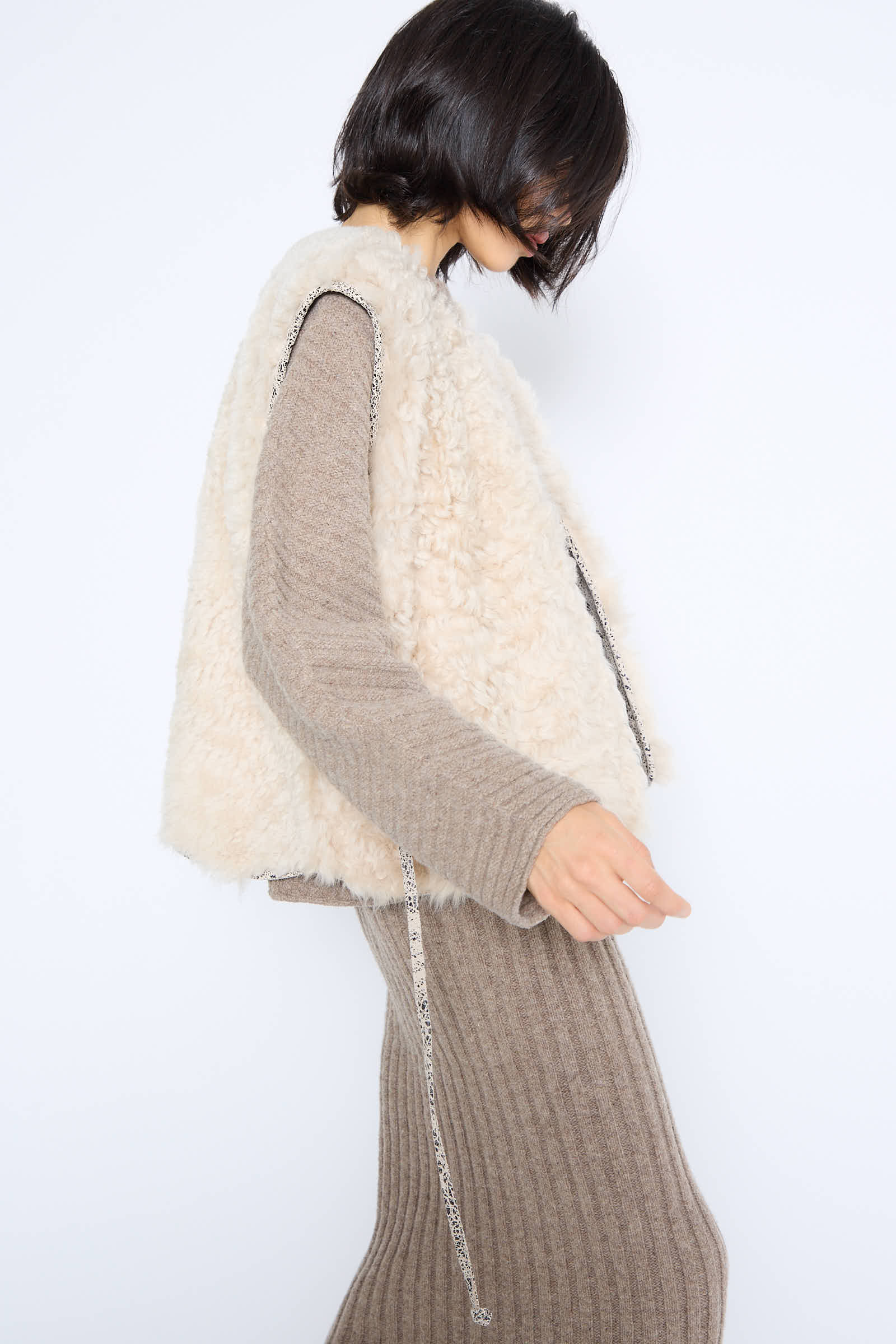 A person wears a beige sweater dress paired with the Transition Vest in Classic by Milena Silvano, showcasing tonal textures against a plain white background.