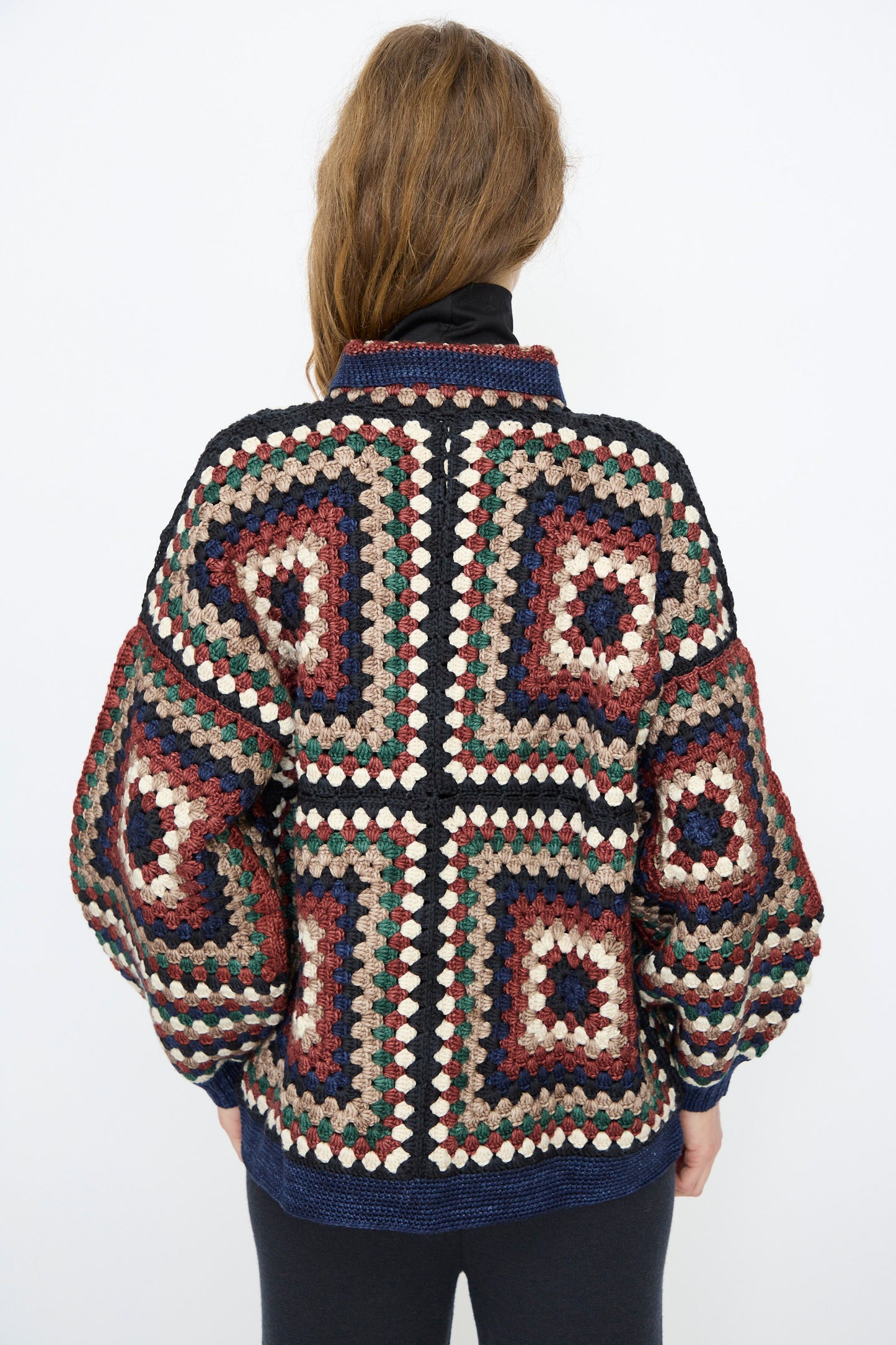A person with long brown hair wears the Misha & Puff Crochet Big Square Jacket in Ink, hand-crocheted from vibrant Merino wool, photographed from the back against a plain white background.