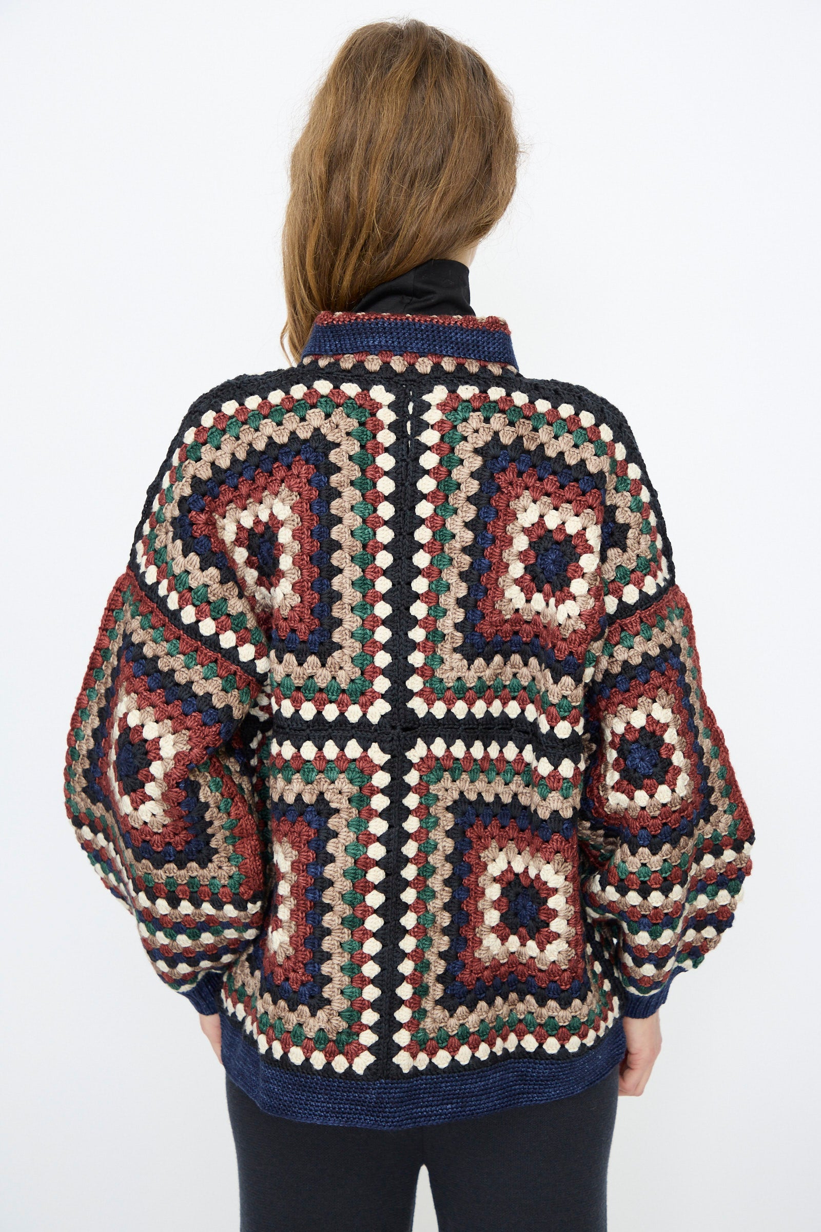 A person with long brown hair wears the Misha & Puff Crochet Big Square Jacket in Ink, hand-crocheted from vibrant Merino wool, photographed from the back against a plain white background.