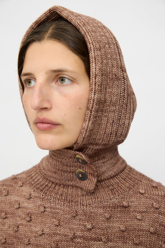 A person wears the Misha & Puff Fisherman Hood in Affogato, a textured brown sweater with a merino cashmere hood and horn button closure, looking slightly to the side against a plain background.