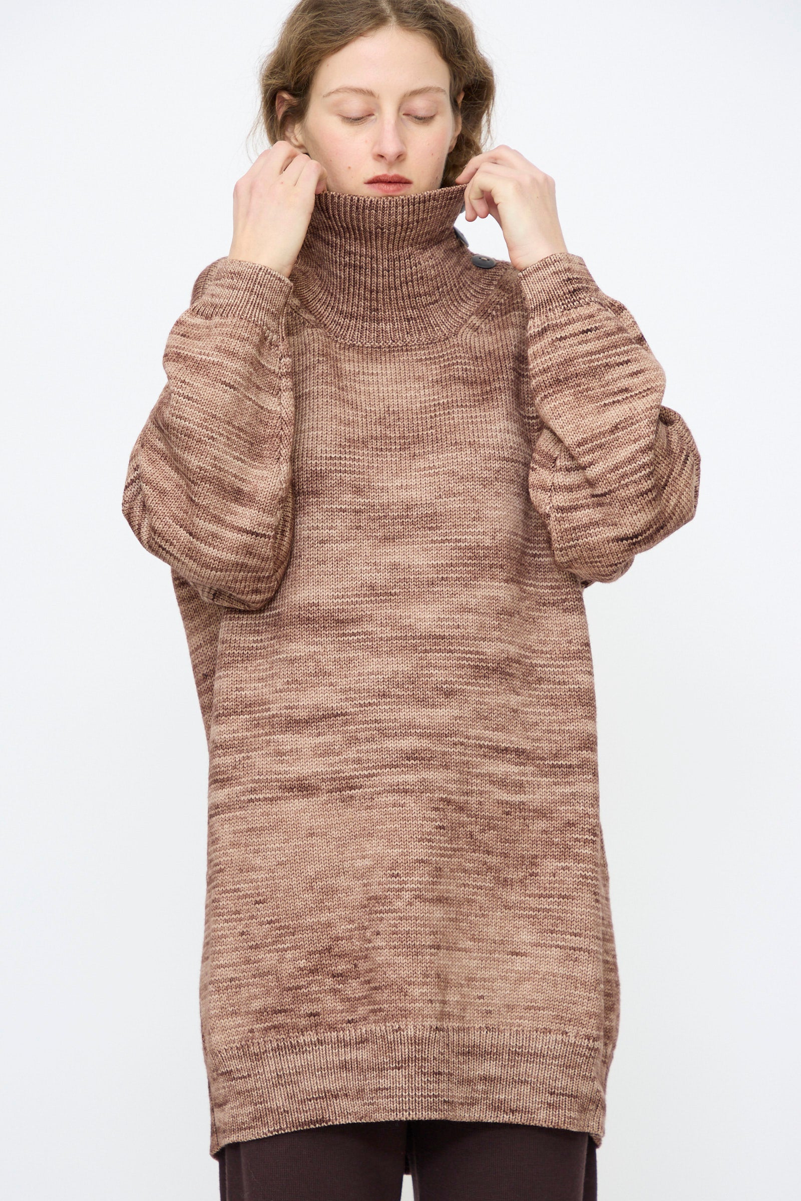 A person wears the Misha & Puff Hutton Dress in Affogato, pulling up the collar with both hands against a plain background.