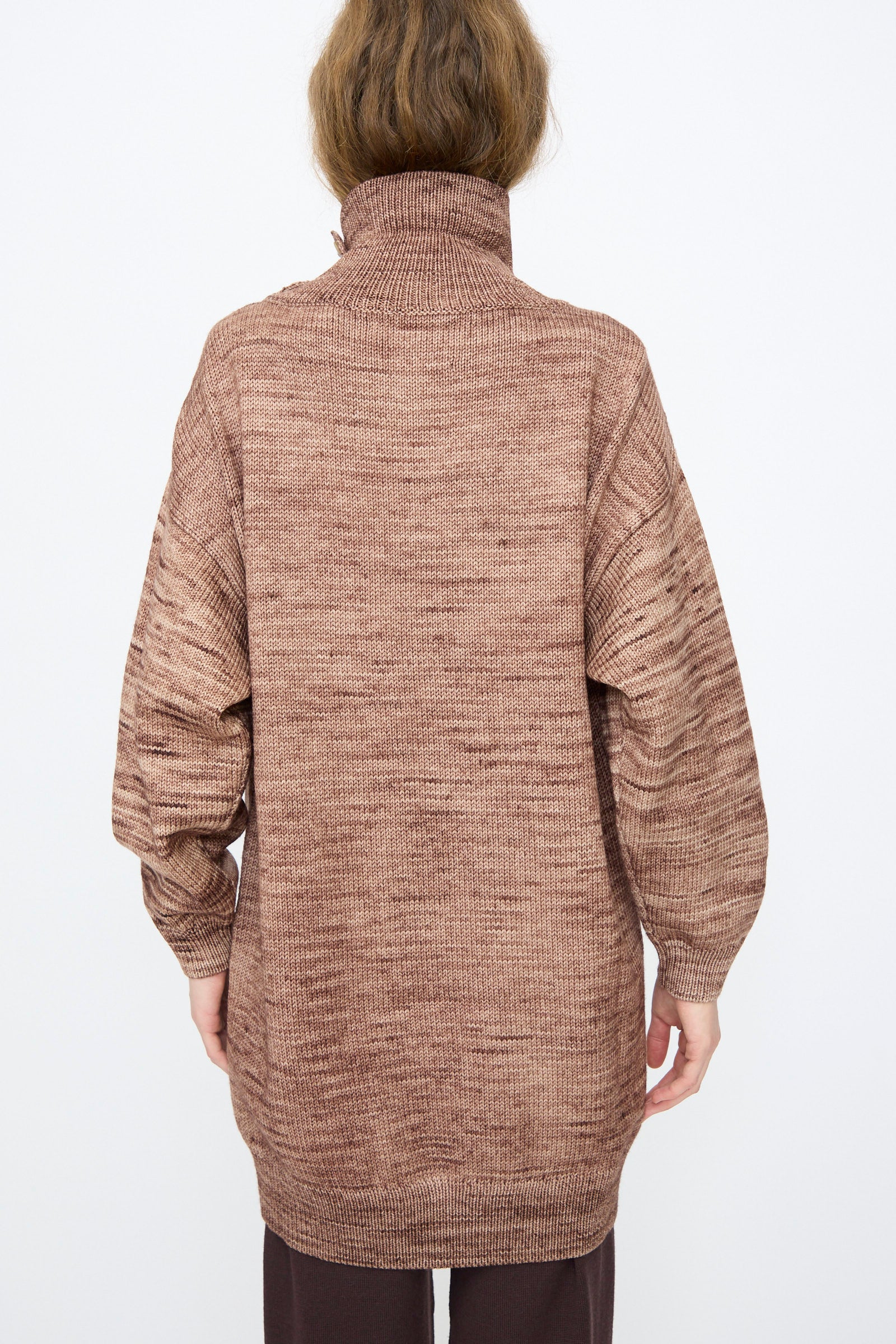 A person stands facing away, wearing the Hutton Dress in Affogato by Misha & Puff—a long, brown Merino wool dress featuring a high neckline, dropped shoulders, and long sleeves.
