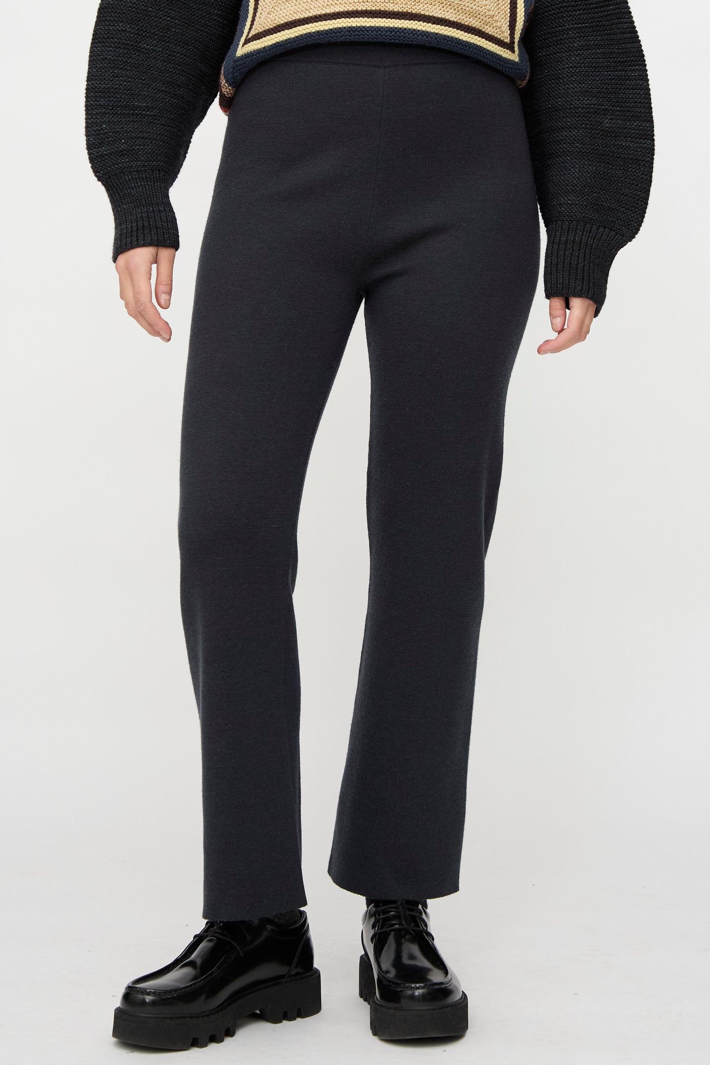 Model wears the Izzy Pant in Carbon by Misha & Puff with black chunky platform shoes and a sweater with textured sleeves, standing against a plain white background.