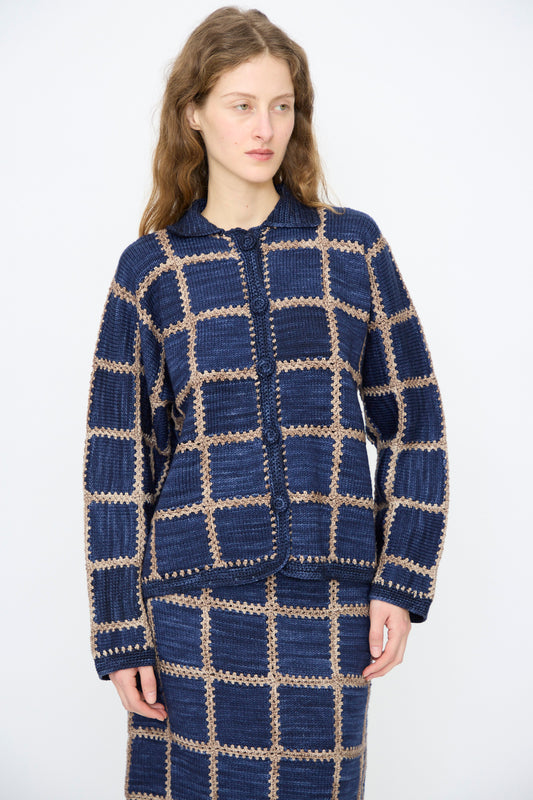 A person wears the Misha & Puff Ladder Square Cardigan in Ink—a blue and beige checkered Merino wool knit—paired with a matching skirt, standing against a plain light background.