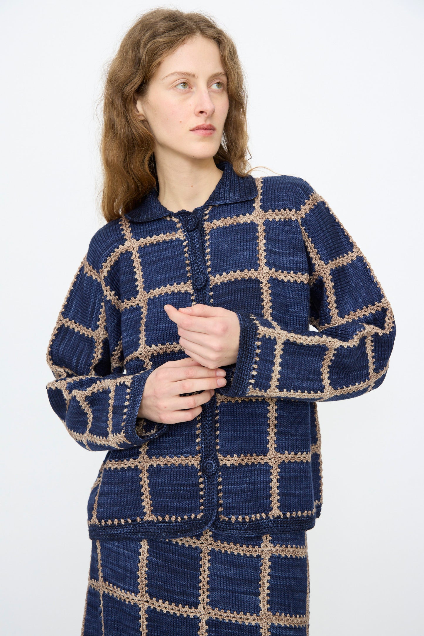 A person wearing the Ladder Square Cardigan in Ink by Misha & Puff stands against a plain light background, looking to the side.