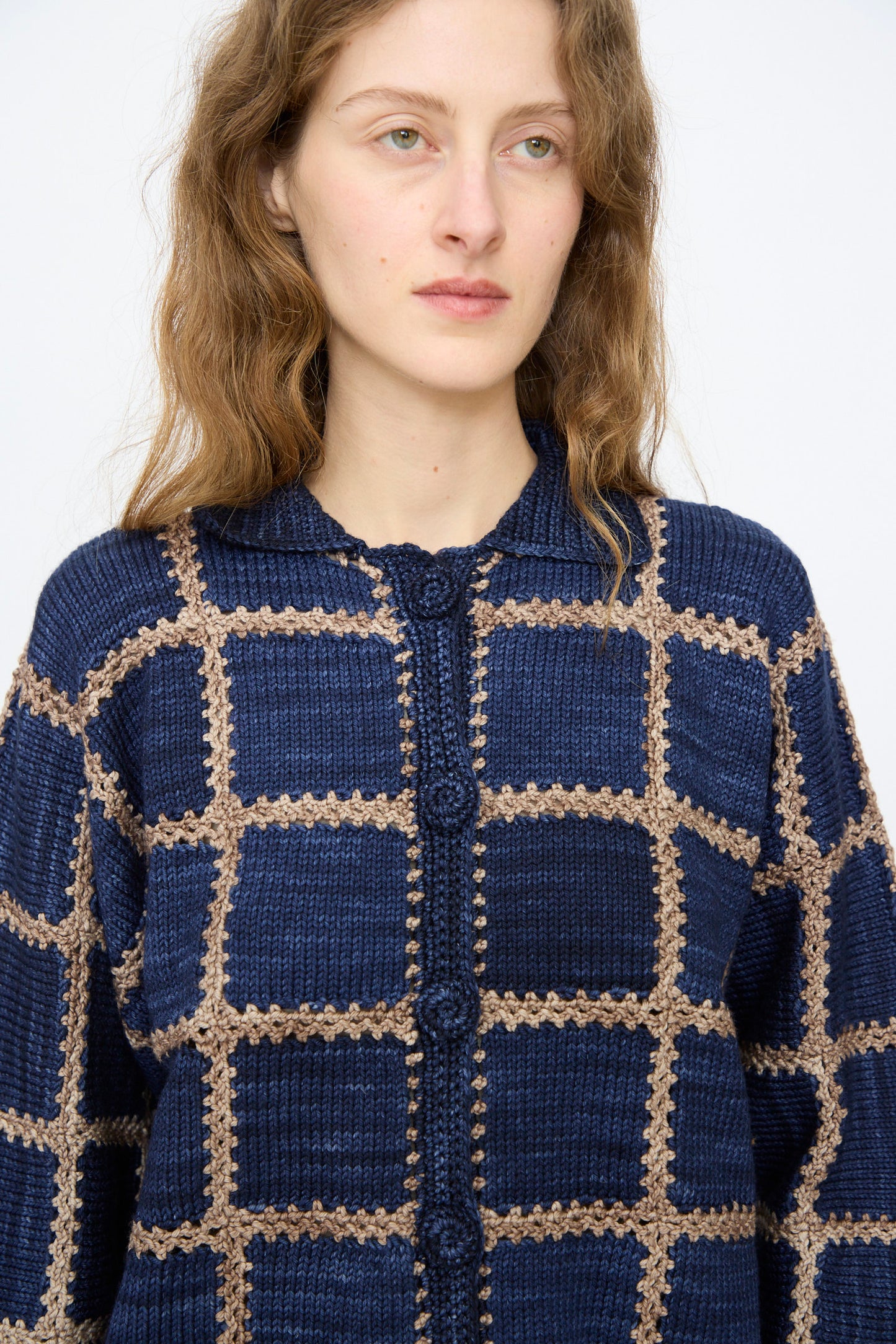 A woman with wavy brown hair wears the Misha & Puff Ladder Square Cardigan in Ink, a blue and beige checkered button-up, standing against a plain light background.