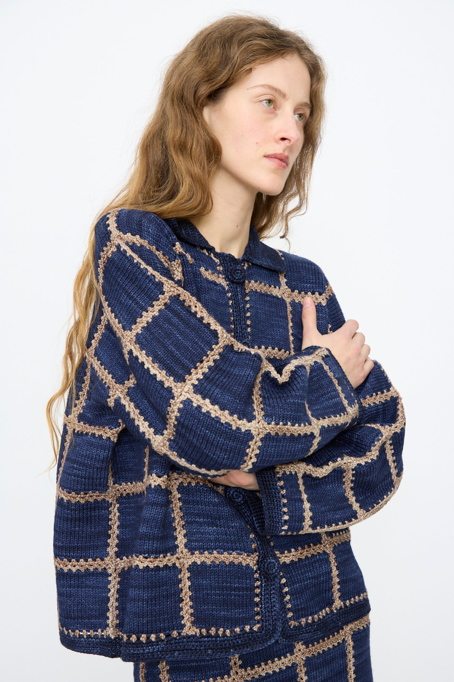A person with long wavy hair wears the Misha & Puff Ladder Square Cardigan in Ink, standing with arms crossed against a plain light background.
