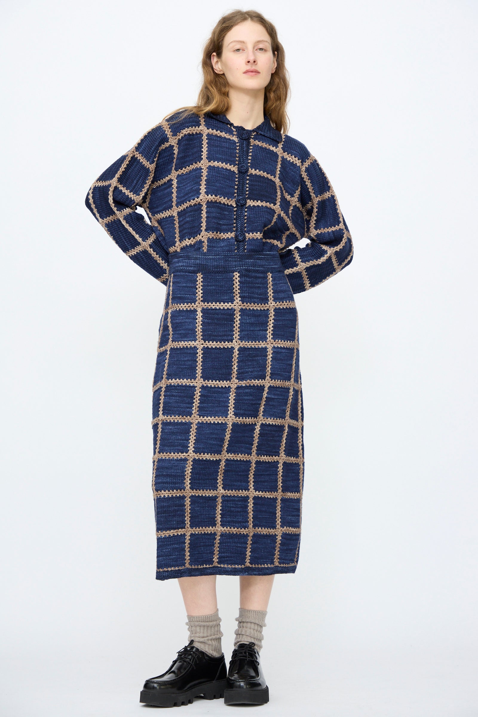 A woman wears the Misha & Puff Ladder Square Skirt in Ink with beige socks and black shoes, standing against a plain light background.