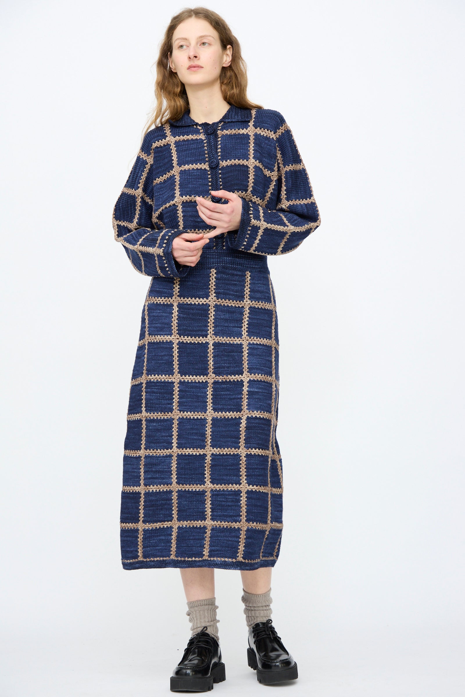 A woman wears the Misha & Puff Ladder Square Skirt in Ink, paired with black platform shoes and beige socks, standing against a plain white background.