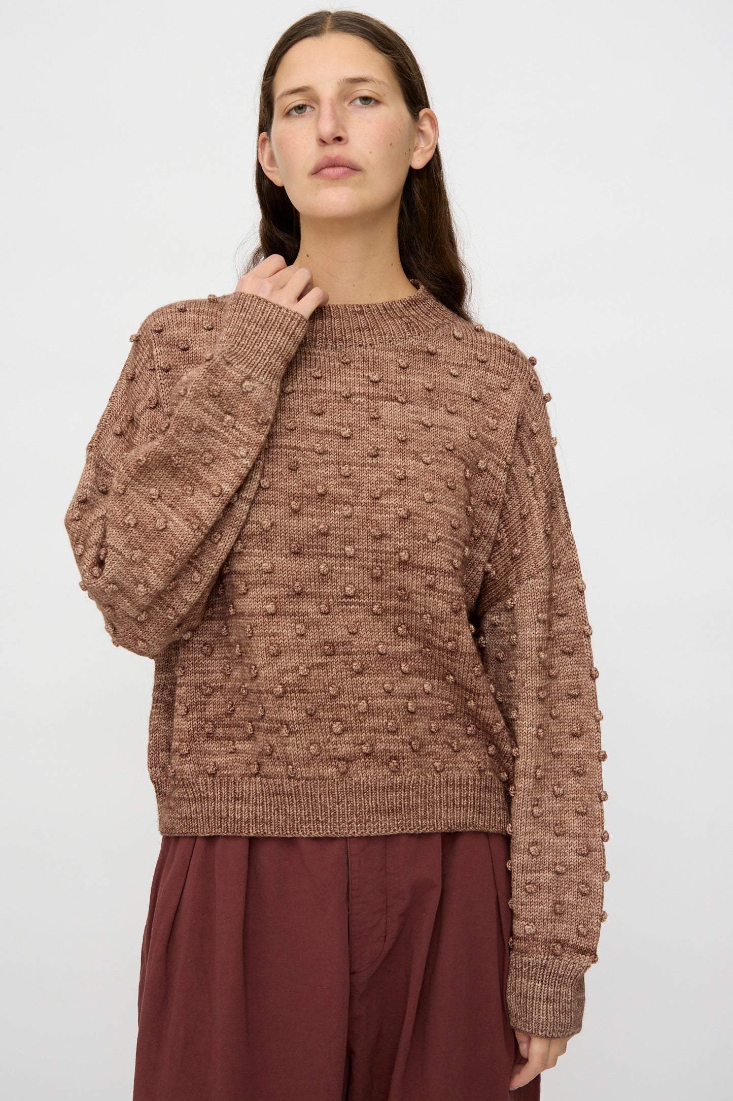 A person wears the Misha & Puff Original Popcorn Sweater in Affogato, featuring a textured raised dot pattern, paired with loose maroon pants against a plain light background.