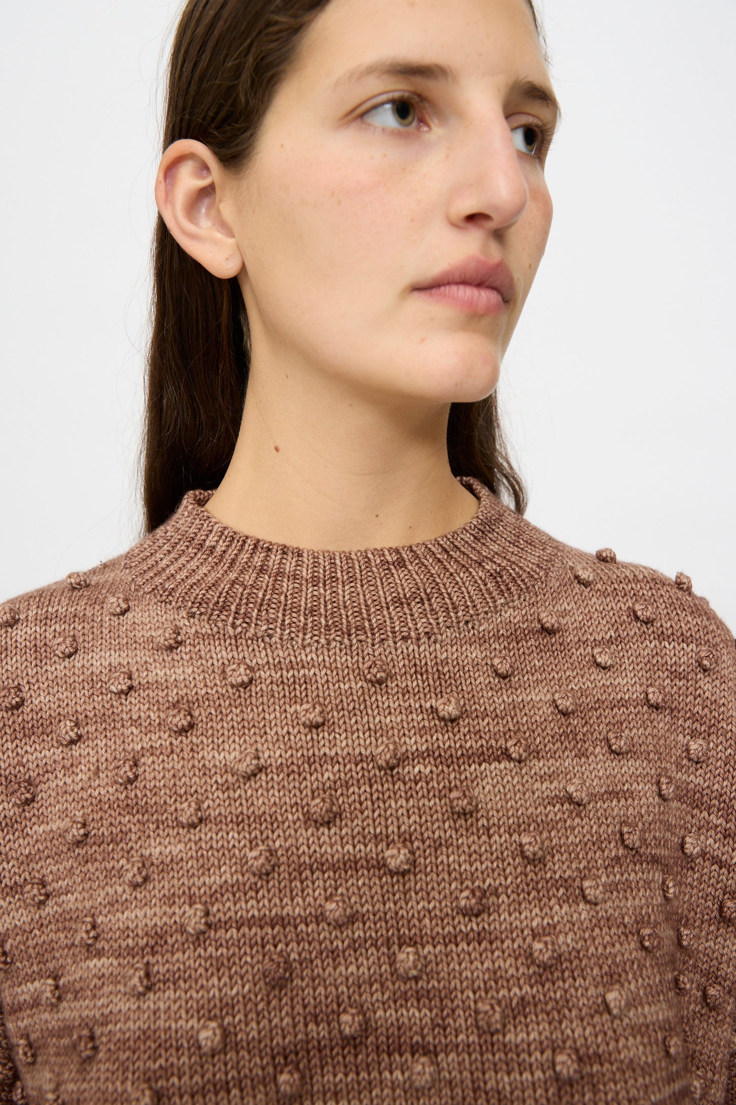 A woman with long brown hair models the Misha & Puff Original Popcorn Sweater in Affogato, featuring raised dot detailing, while looking slightly to the side against a plain light background.