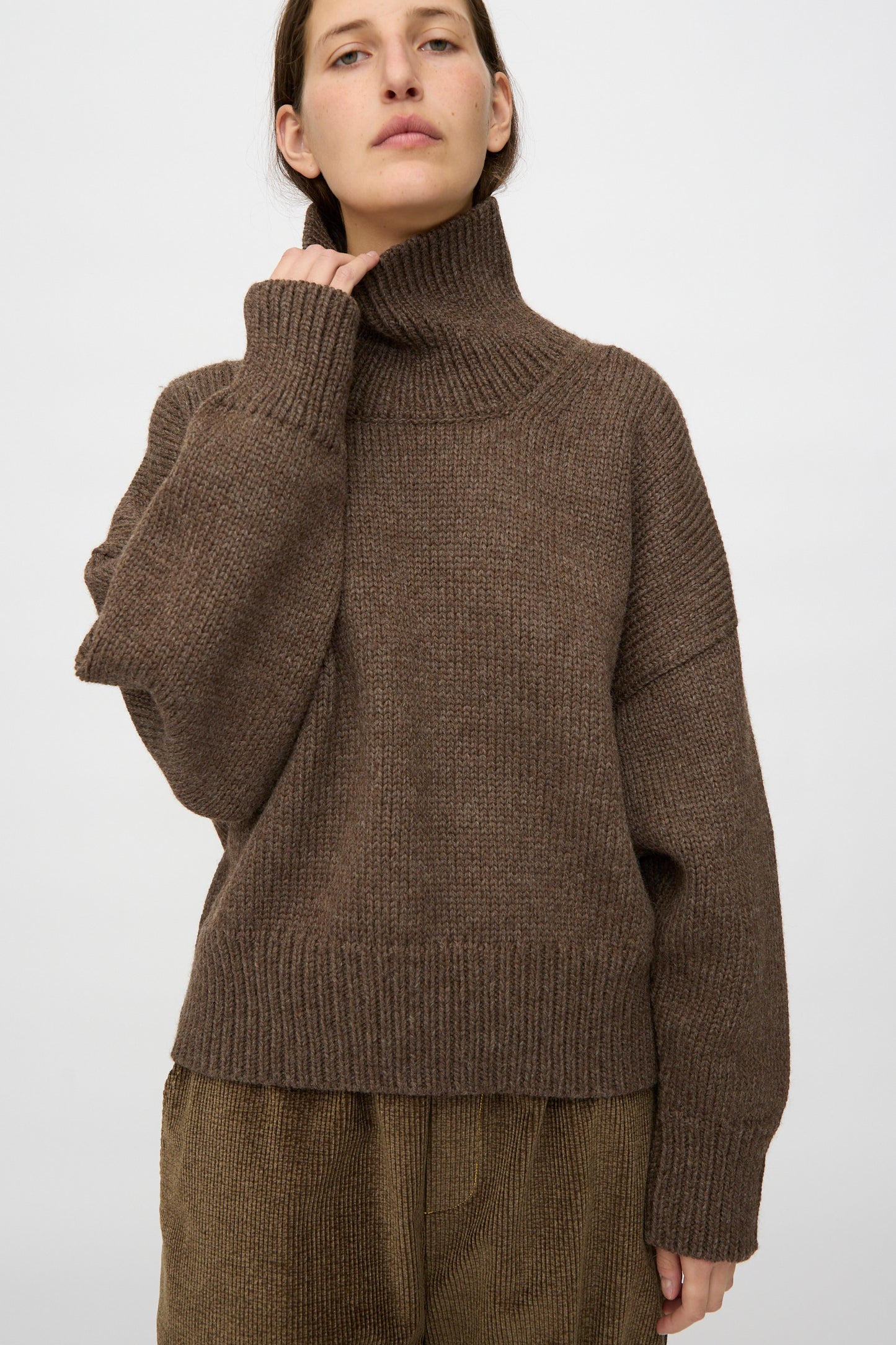 A person wears the Misha & Puff Turtleneck Sweater in Oak with matching brown pants, standing against a plain light background.