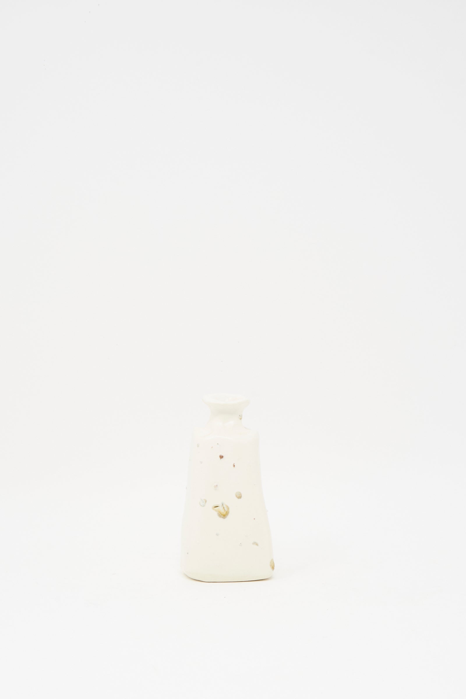 The Carved Bud Vase I by MONDAYS is a small white ceramic vase with a narrow neck and subtle speckles, crafted from clay and photographed on a plain white background, adding Brooklyn style to any space.