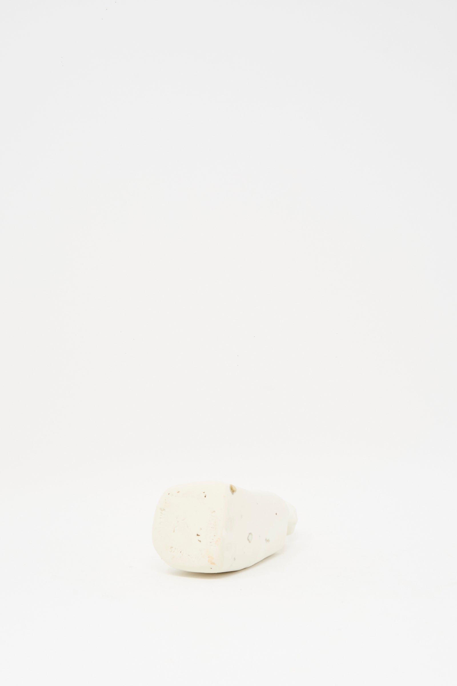 The Carved Bud Vase I by MONDAYS features a small, white, irregular shape and sits on a plain white surface with a white background, embodying a minimalist Brooklyn aesthetic.