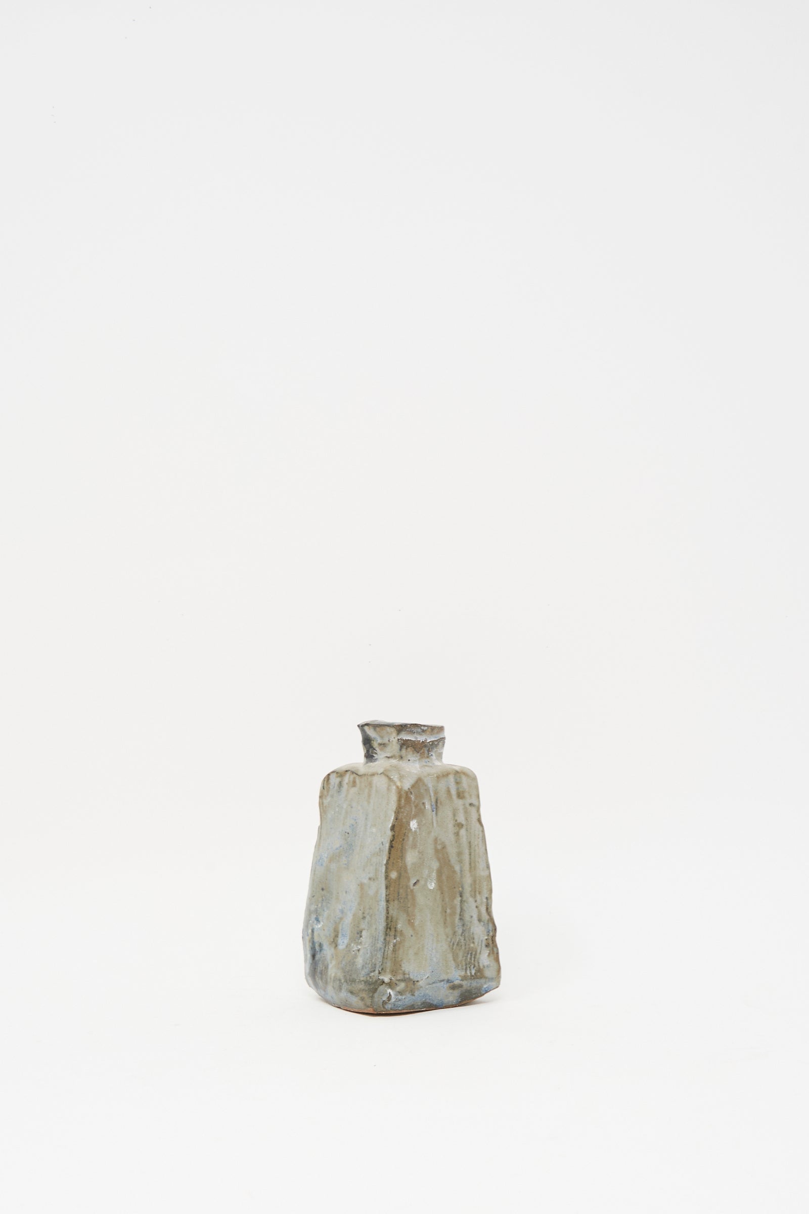 The MONDAYS Carved Bud Vase II is a small, handmade clay vase with an irregular shape and rough, textured surface in earthy tones, displayed against a plain white background.