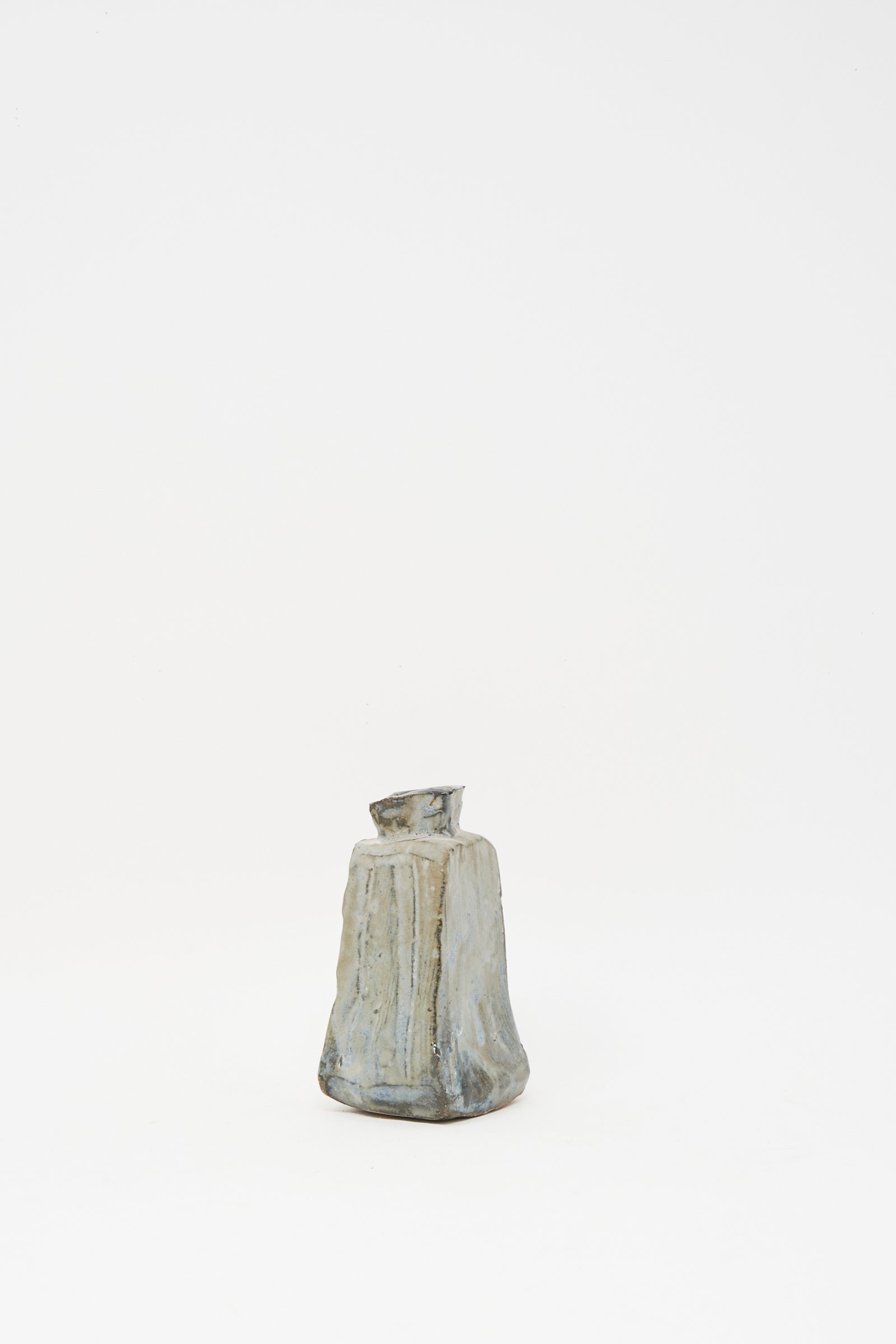 The Carved Bud Vase II by MONDAYS is a small, irregularly shaped clay vase with a narrow, slightly tilted opening, displayed on a white background.