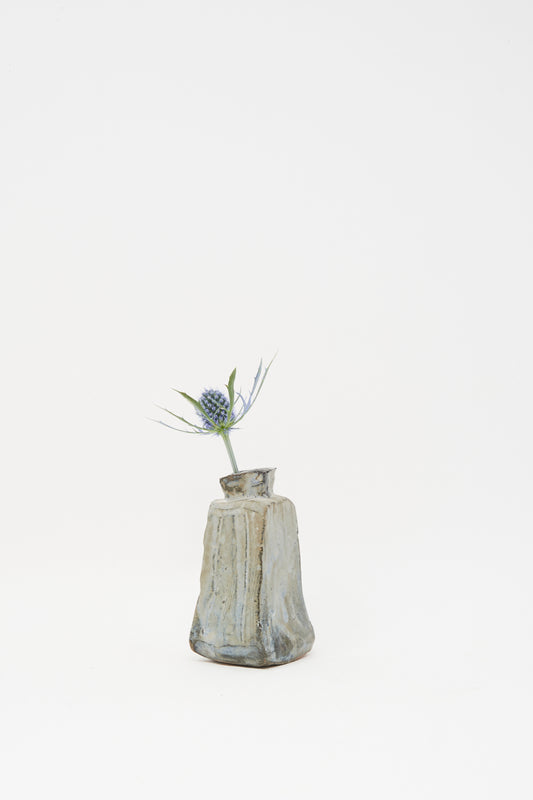 The Carved Bud Vase II by MONDAYS displays a single spiky thistle flower against a plain white backdrop, capturing minimalist Brooklyn charm.