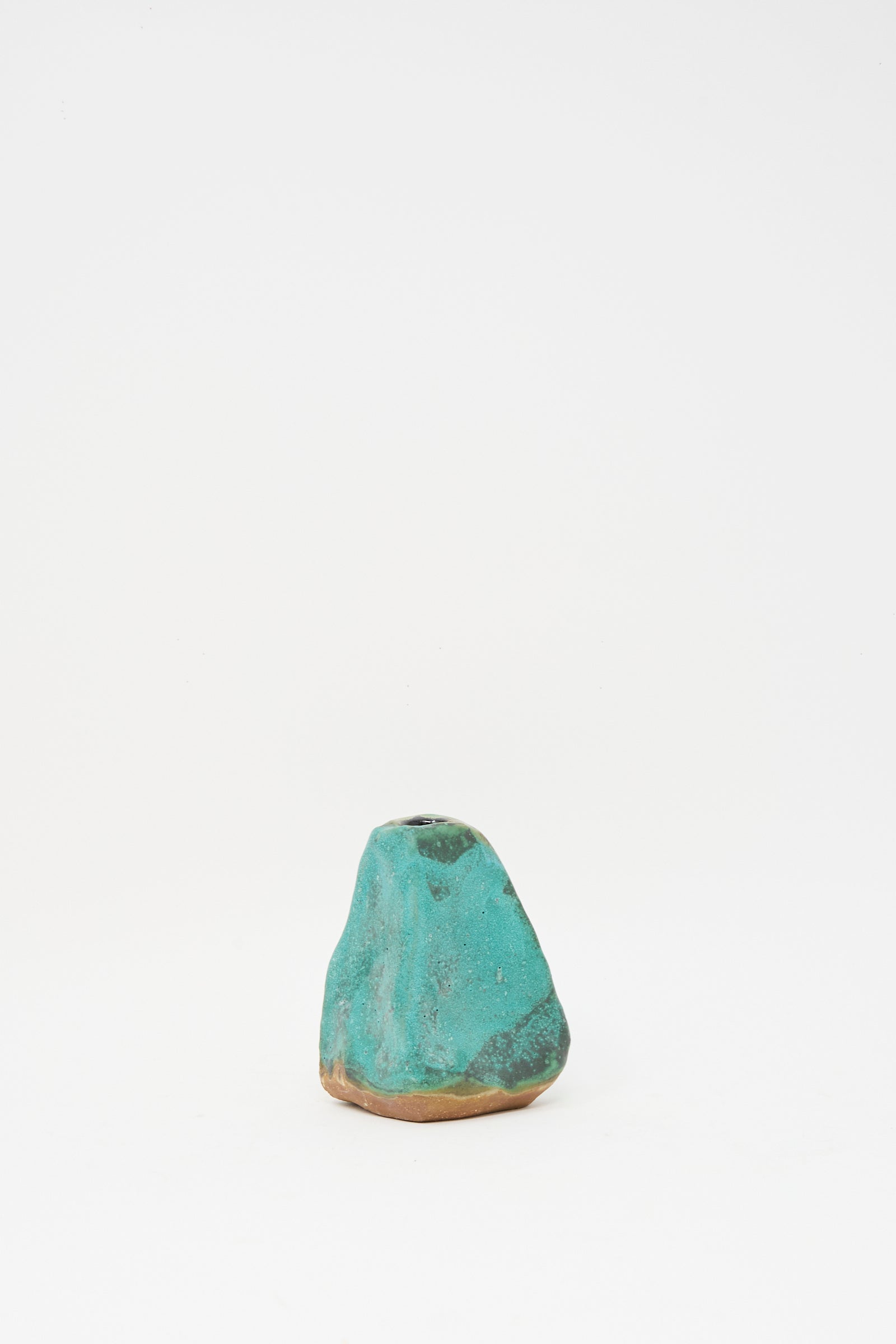 The Carved Bud Vase III by MONDAYS is a small, irregularly shaped clay vase with a textured turquoise surface and a brown base, shown against a plain white background.