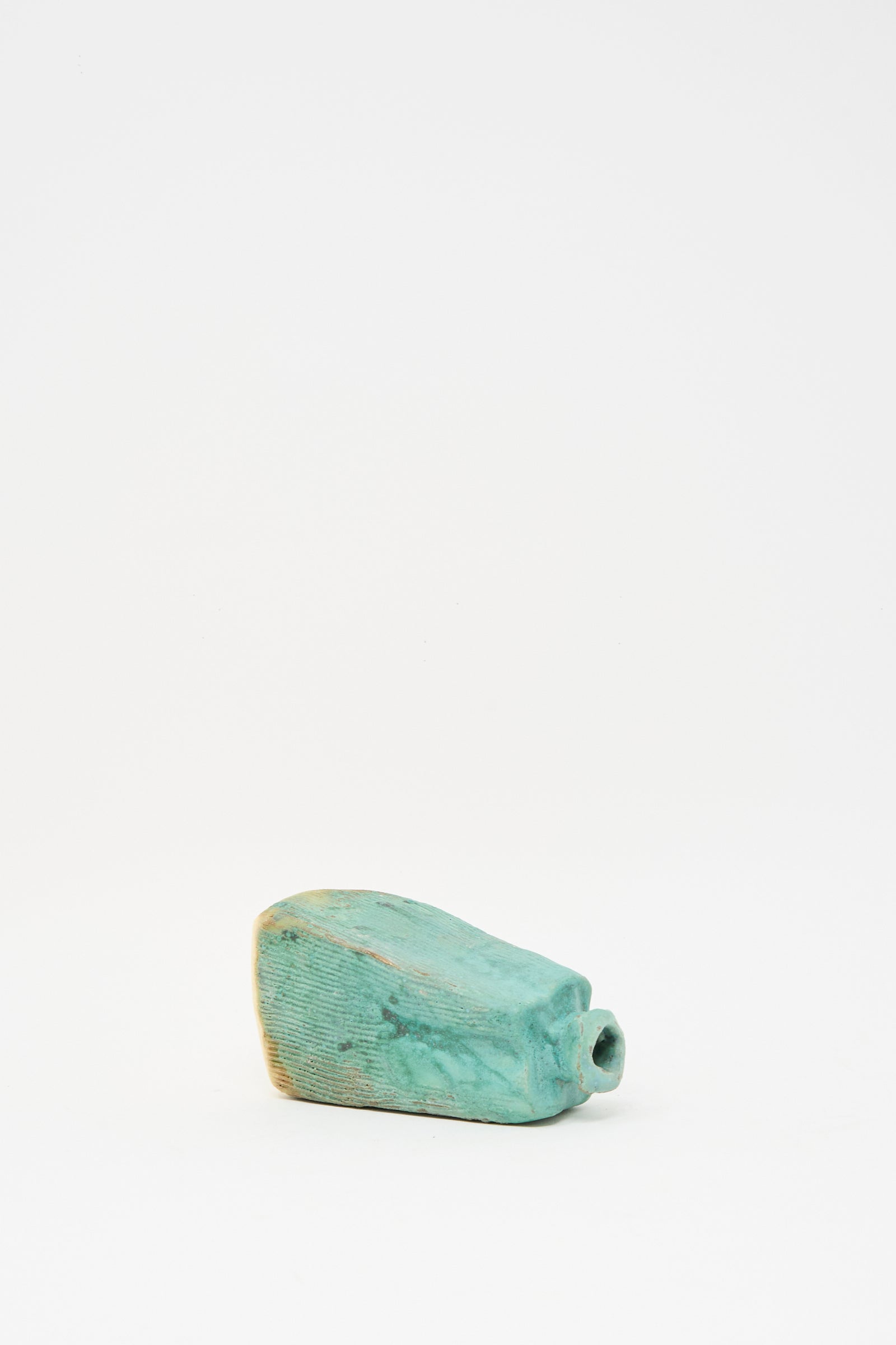 The Carved Bud Vase IV by MONDAYS is a turquoise ceramic bud vase from Brooklyn, featuring an irregular rectangular shape, subtle rib pattern, and small cylindrical opening, shown against a plain white background.