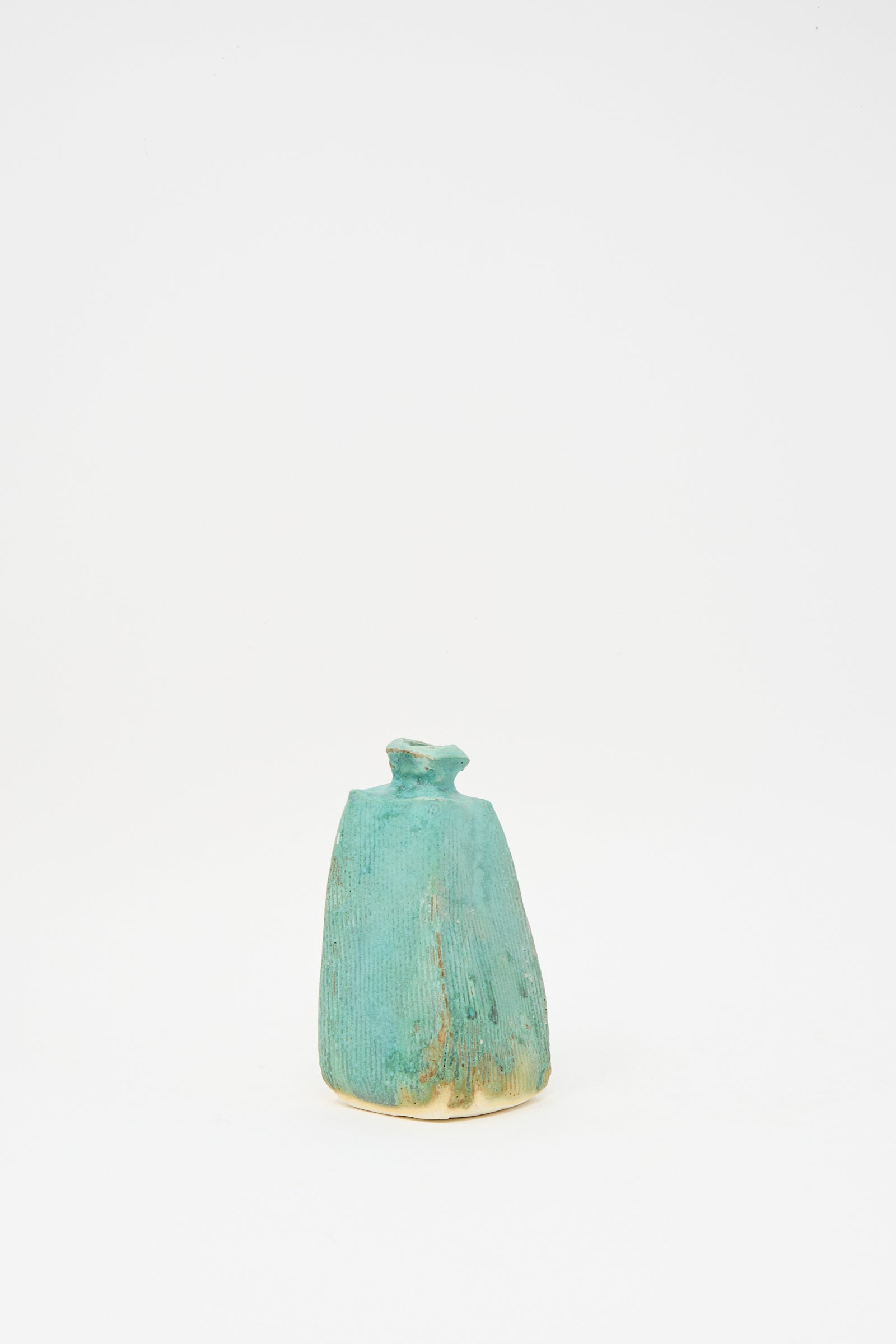 The Carved Bud Vase IV by MONDAYS is a small, ribbed bud vase with a narrow neck and an irregular turquoise shape, crafted in Brooklyn and shown against a plain white background.
