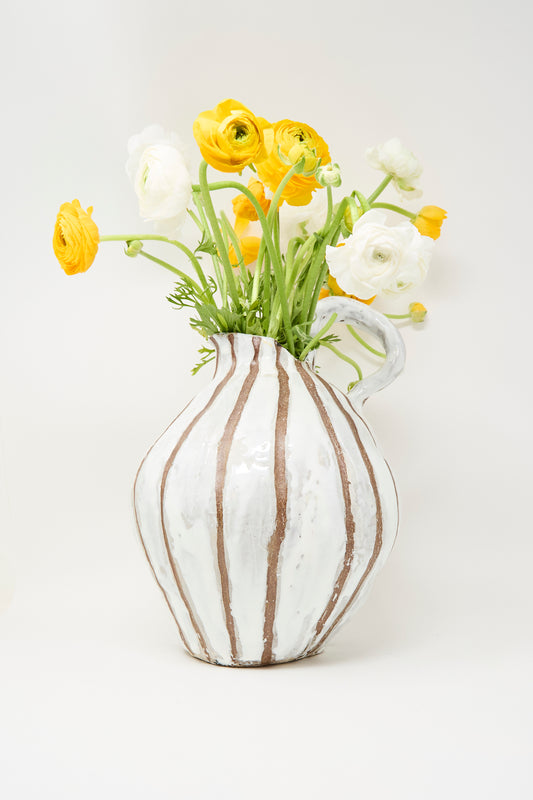 The MONDAYS Coil-built Glazed Stoneware Striped Pitcher Vase holds yellow and white ranunculus flowers, displayed against a plain white background.