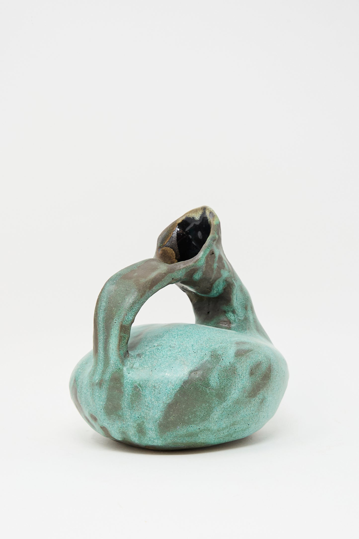 The MONDAYS Glazed Stoneware Pitcher Vase in Green features a turquoise glaze, a round body, curved handle, slanted opening, and an irregular organic shape. Each vase is hand-built for a unique look.