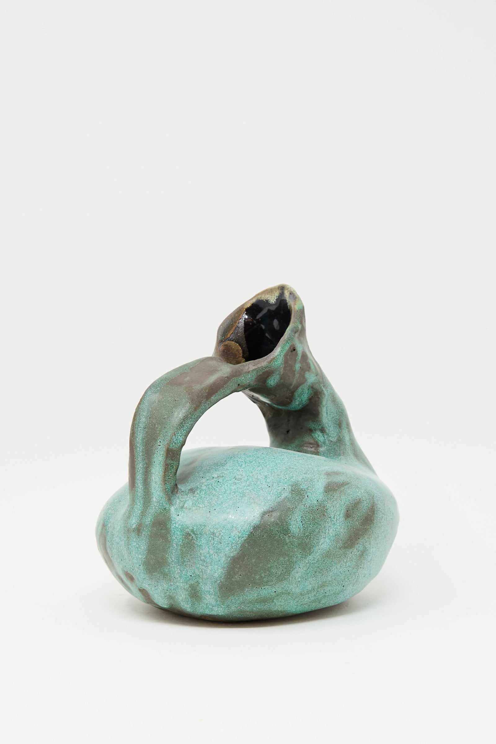 The MONDAYS Glazed Stoneware Pitcher Vase in Green features a turquoise glaze, a round body, curved handle, slanted opening, and an irregular organic shape. Each vase is hand-built for a unique look.