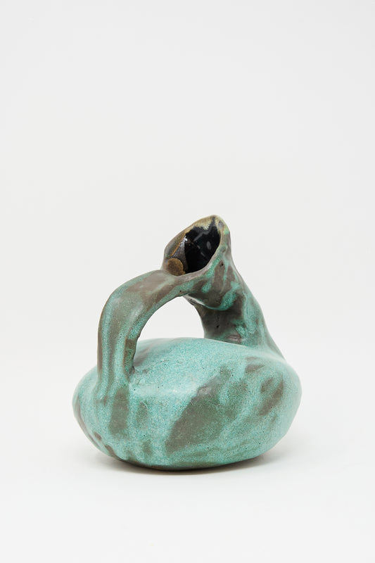 The MONDAYS Glazed Stoneware Pitcher Vase in Green features a turquoise glaze, a round body, curved handle, slanted opening, and an irregular organic shape. Each vase is hand-built for a unique look.