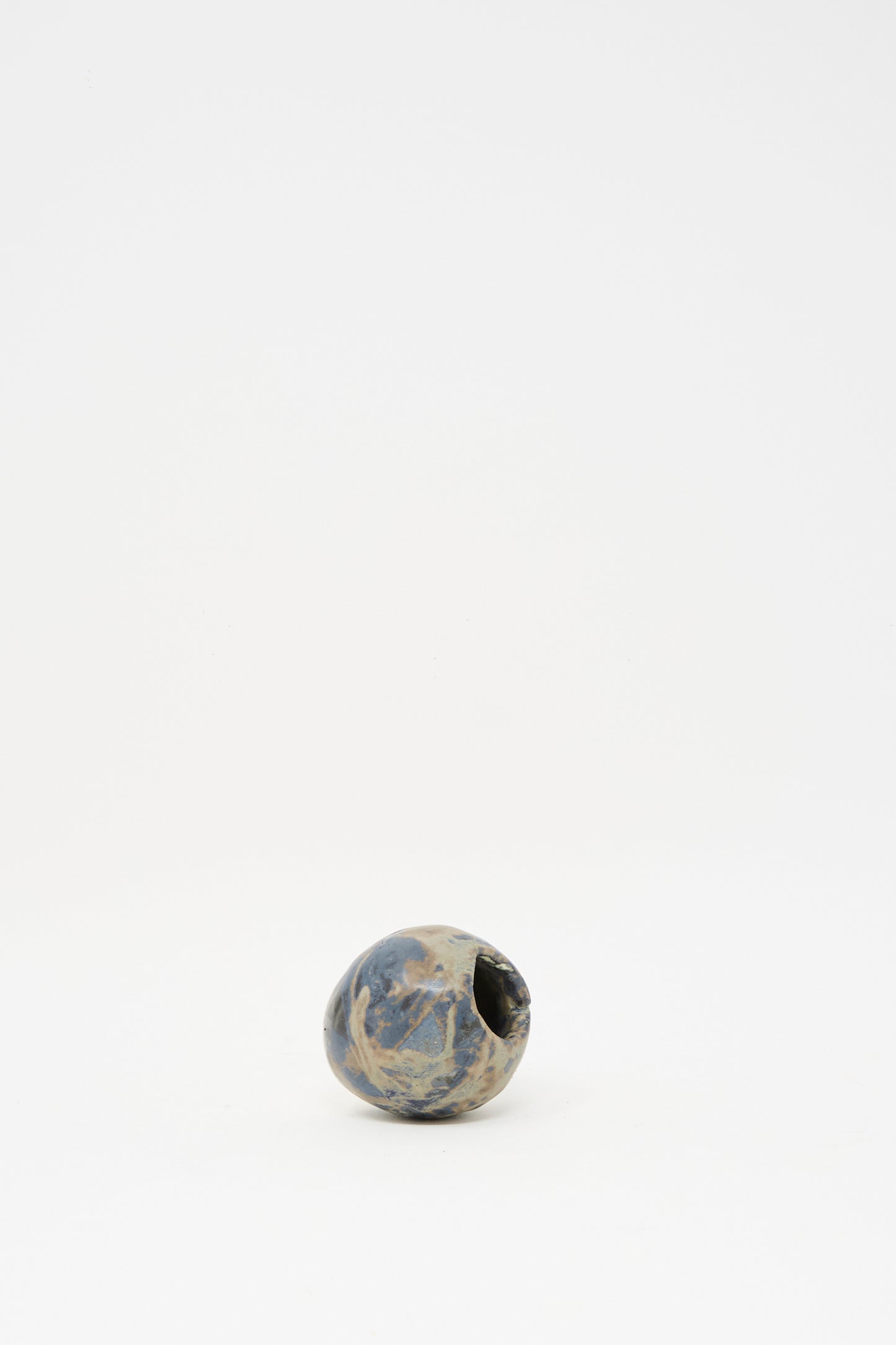 The MONDAYS Mini Bud Vase I is a small, round, hand-built porcelain vase featuring a subtle blue glaze and a narrow opening, showcased on a plain white background.