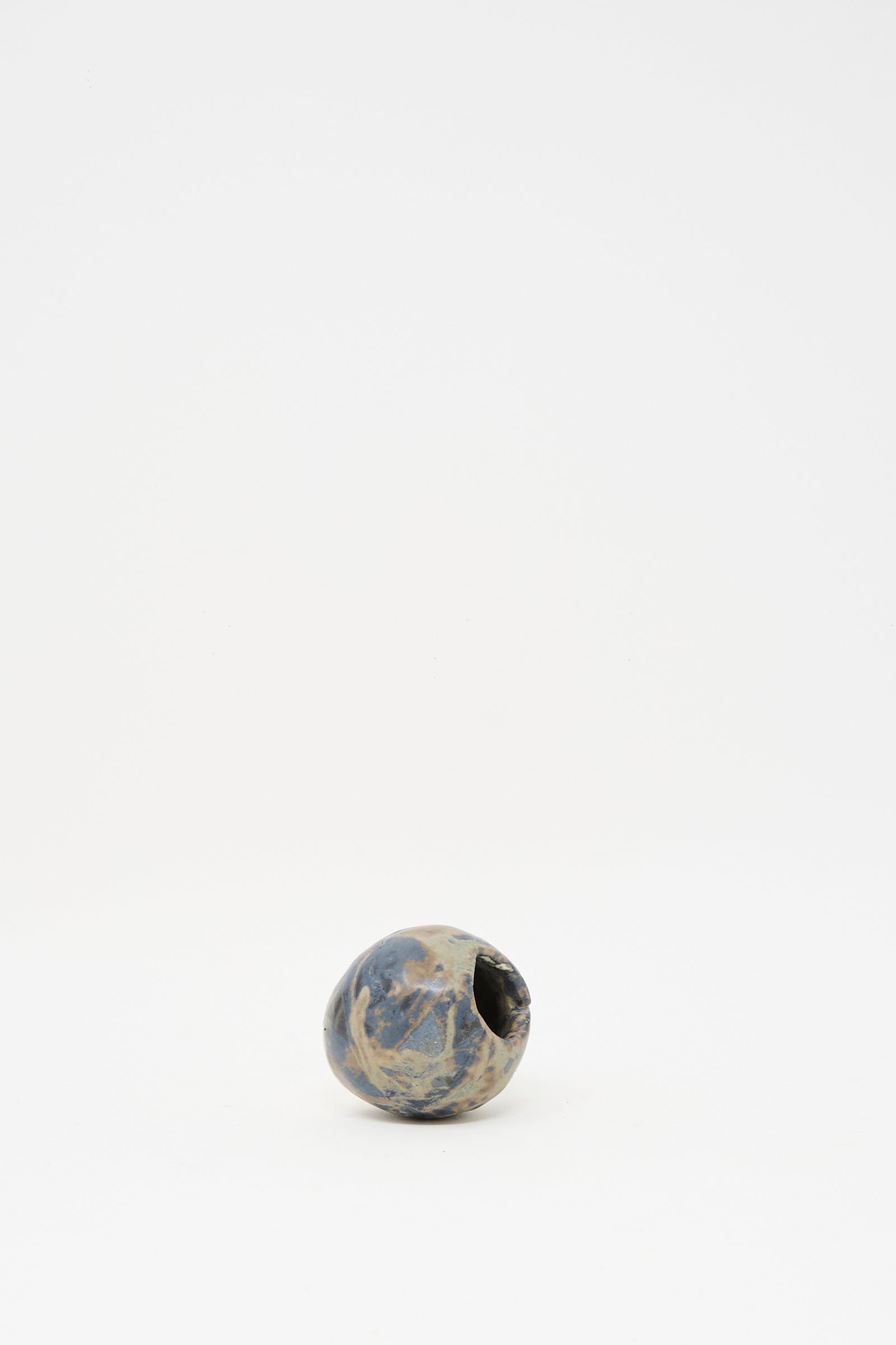 The MONDAYS Mini Bud Vase I is a small, round, hand-built porcelain vase featuring a subtle blue glaze and a narrow opening, showcased on a plain white background.