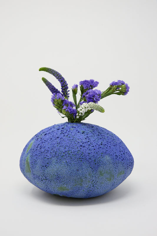 A MONDAYS Moon Vase in Blue Glazed Stoneware is adorned with purple flowers.