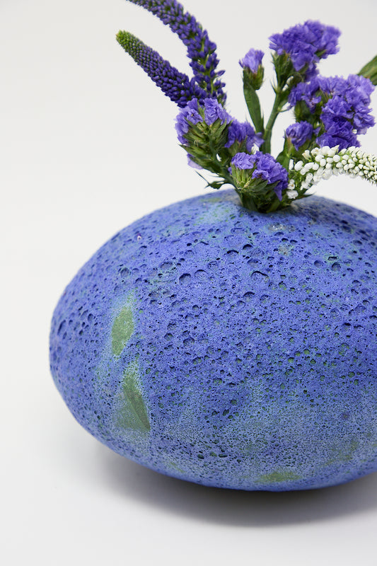 A hand-built Moon Vase in Blue Glazed Stoneware, displaying purple flowers by MONDAYS.