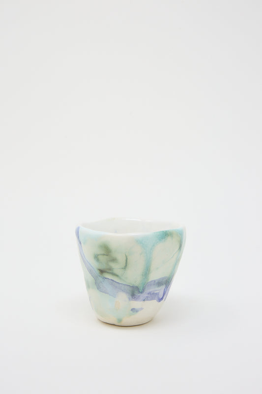 A small MONDAYS blue and white porcelain tumbler sits on a white surface.