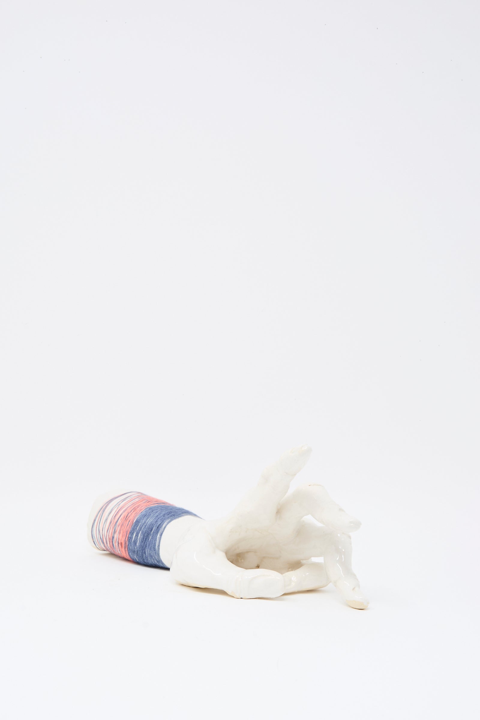The Ceramic Hand Sculpture with Pink and Blue Thread by Monty J lies on its side against a plain white background, handmade in Brooklyn.