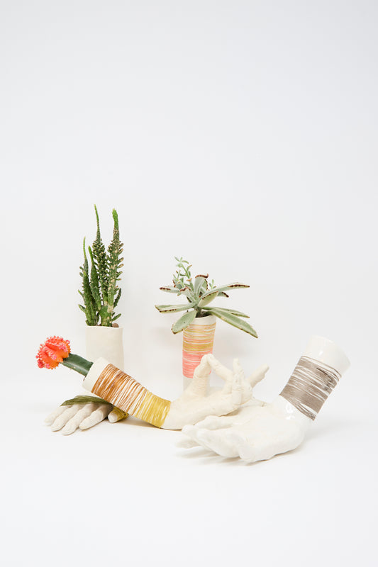 The Ceramic Hand Sculpture with Yellow and Orange Thread by Monty J cradles a succulent and a cactus with a red flower, set against a plain white background.