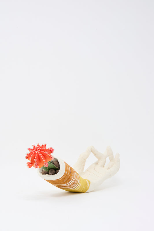A small red cactus sits in the Monty J Ceramic Hand Sculpture with Yellow and Rust Thread, handmade in Brooklyn and shaped in an "OK" gesture, set against a plain white background.