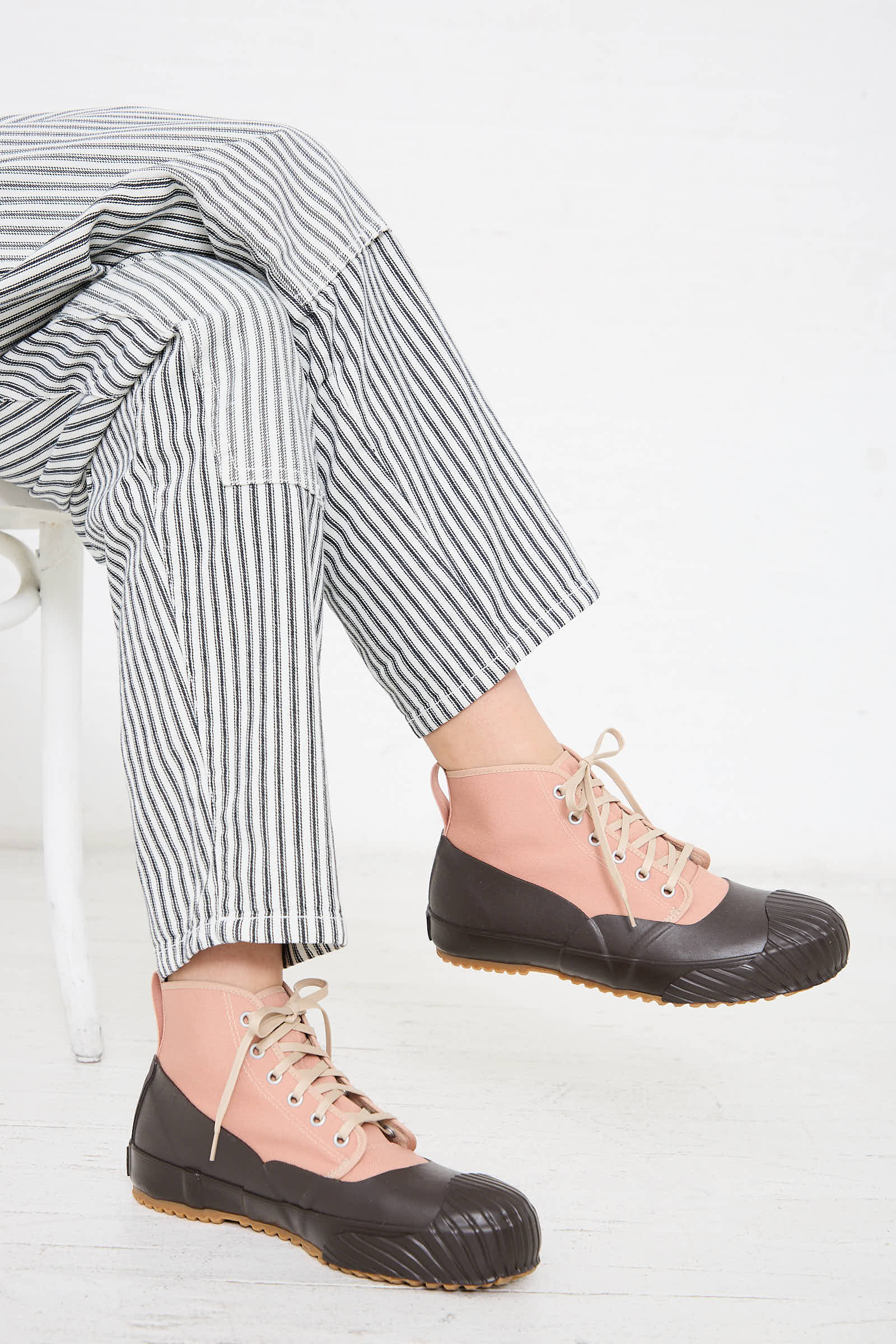 Person seated on a white chair, wearing black and white striped pants and Moonstar Alweather Sneaker in Coral.