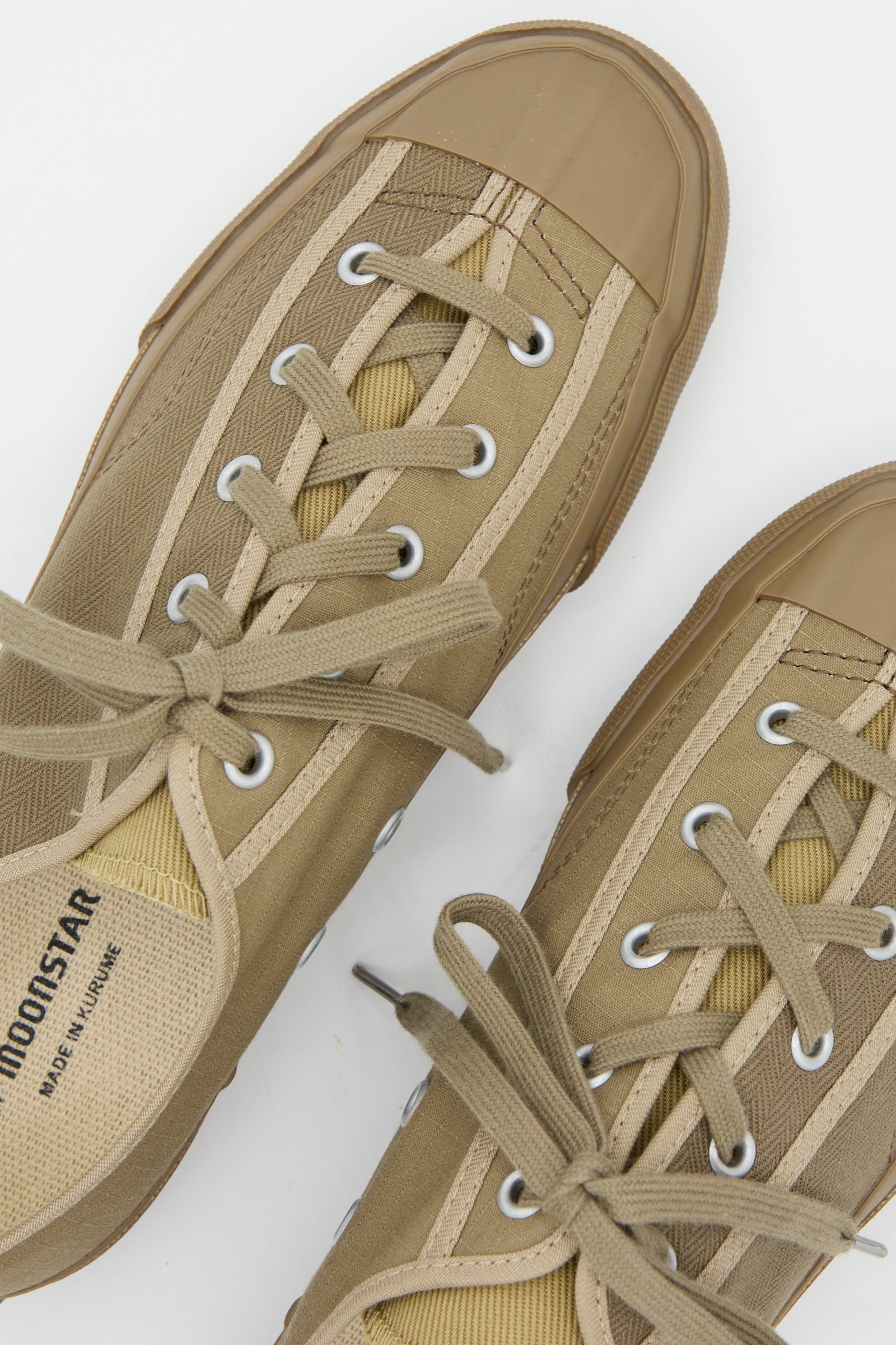 Close-up of Gym Classic in Beige Multi by Moonstar, featuring tan lace-up sneakers with durable canvas, rubber toe caps, and metal eyelets. Branding visible on the tongue of this low-top design.